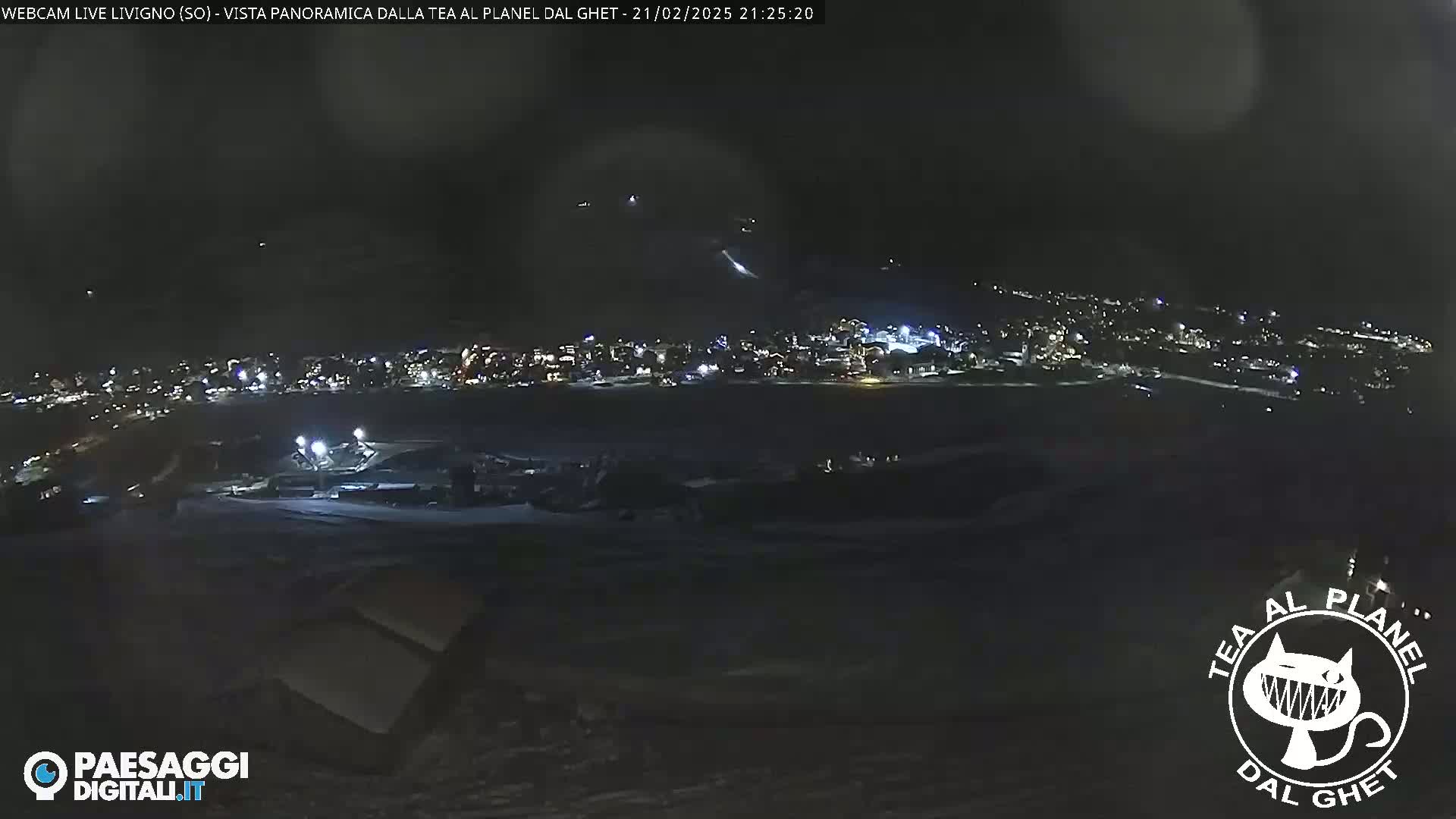A nighttime, panoramic view of a snow-covered town illuminated by lights, under a dark, possibly slightly overcast sky.