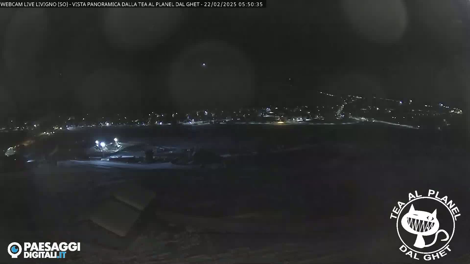 A nighttime, panoramic view of a snow-covered landscape with a dimly lit town in the distance.