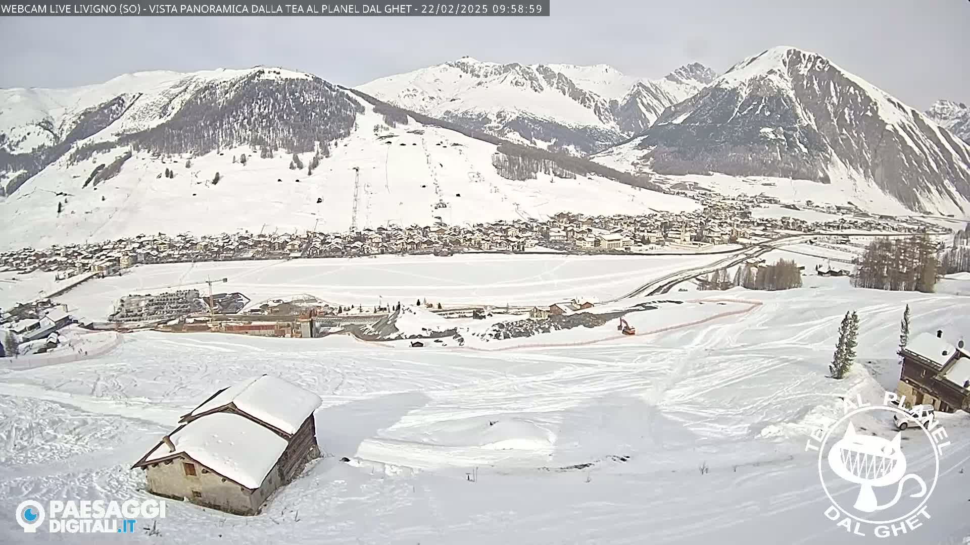 A snow-covered mountain valley town is visible below a mountain range under a mostly cloudy sky.