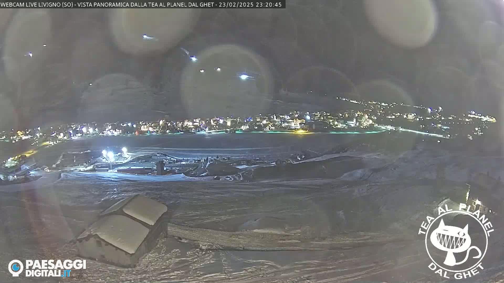 A nighttime, snowy landscape shows a town's lights in the distance, with a few lights visible in the sky.