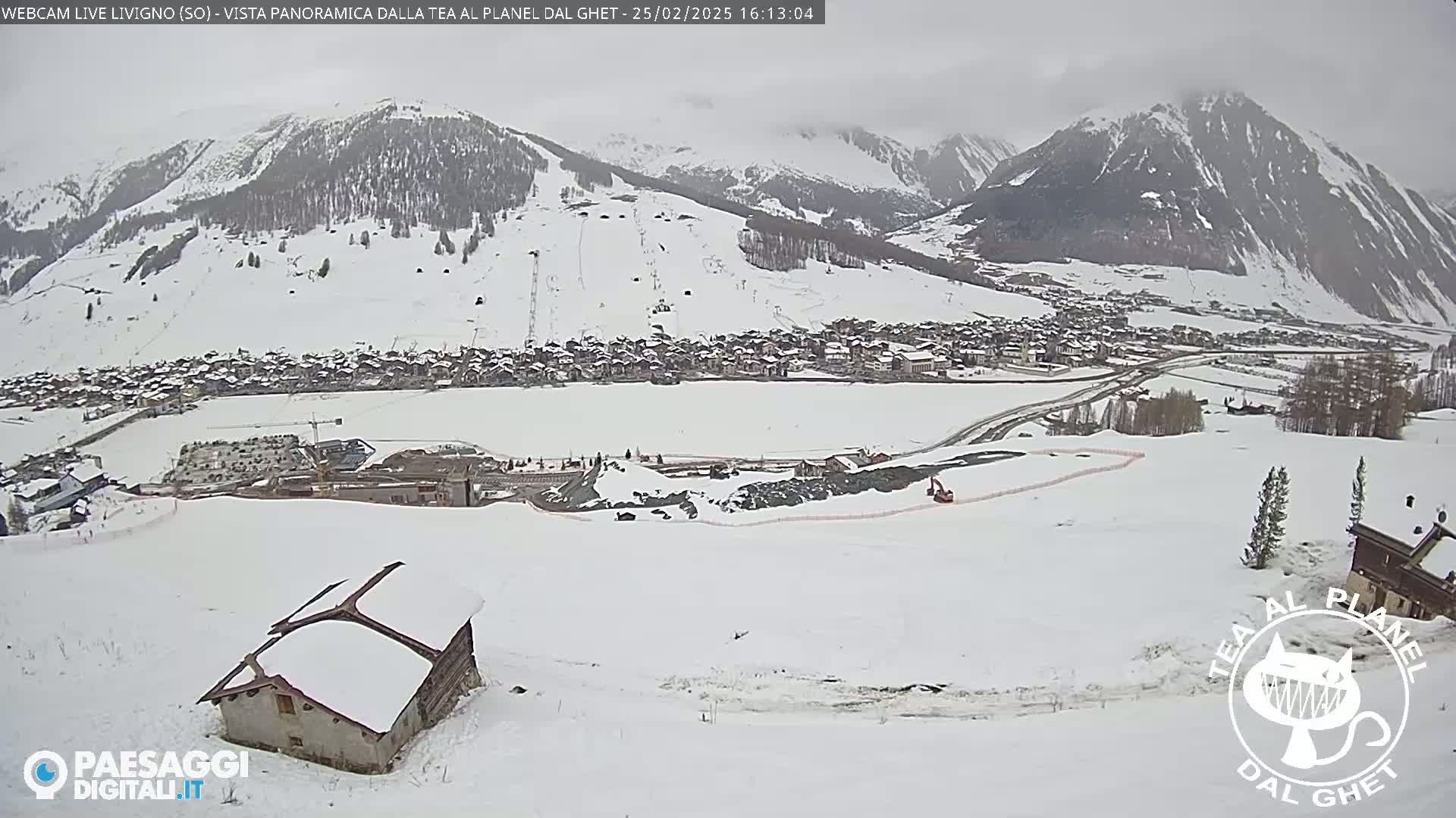 A snow-covered mountain village is seen from a snowy hillside, with overcast skies and a partially visible construction site.