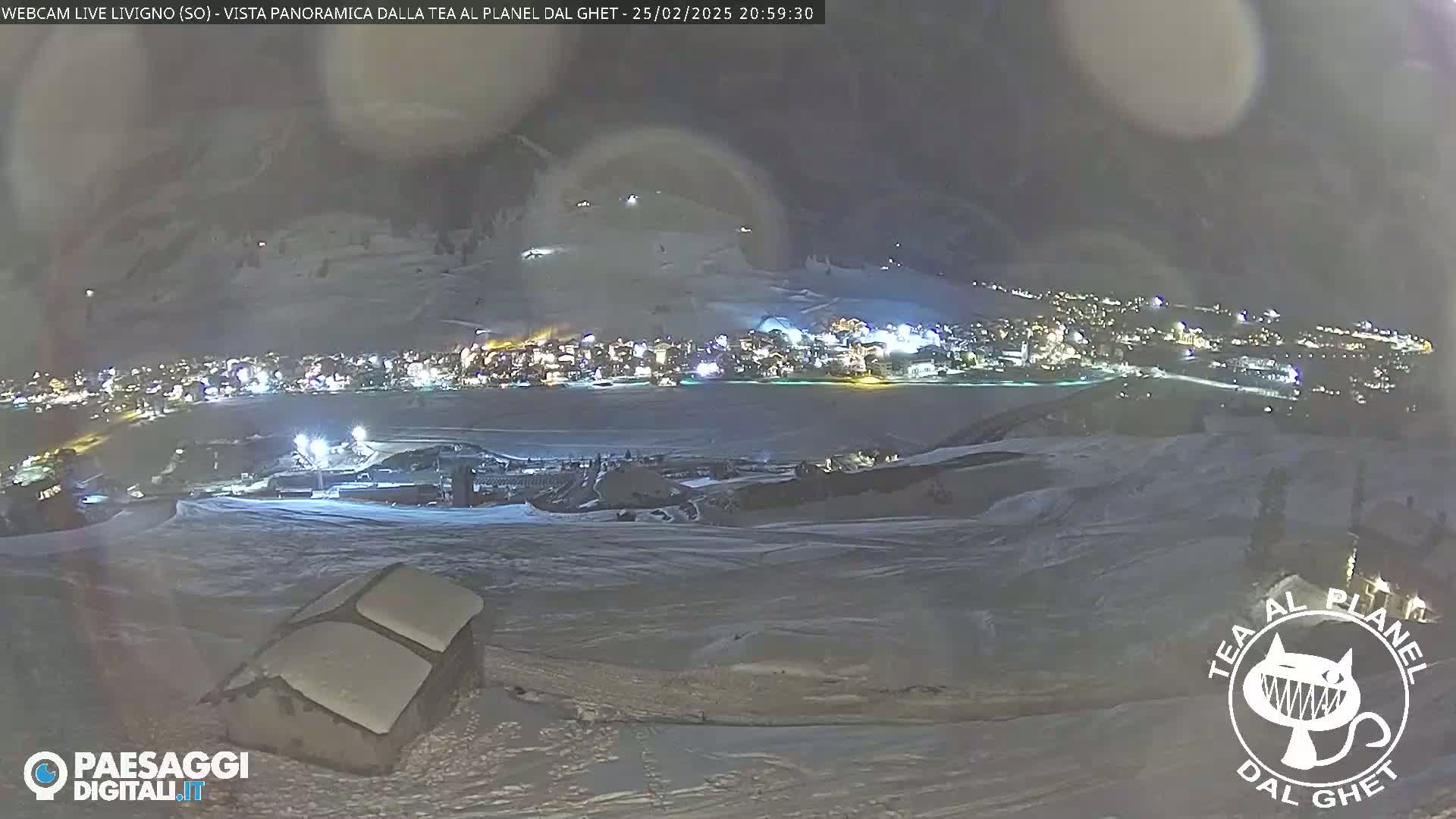 A nighttime, snowy landscape shows a town illuminated below, viewed from a high vantage point.