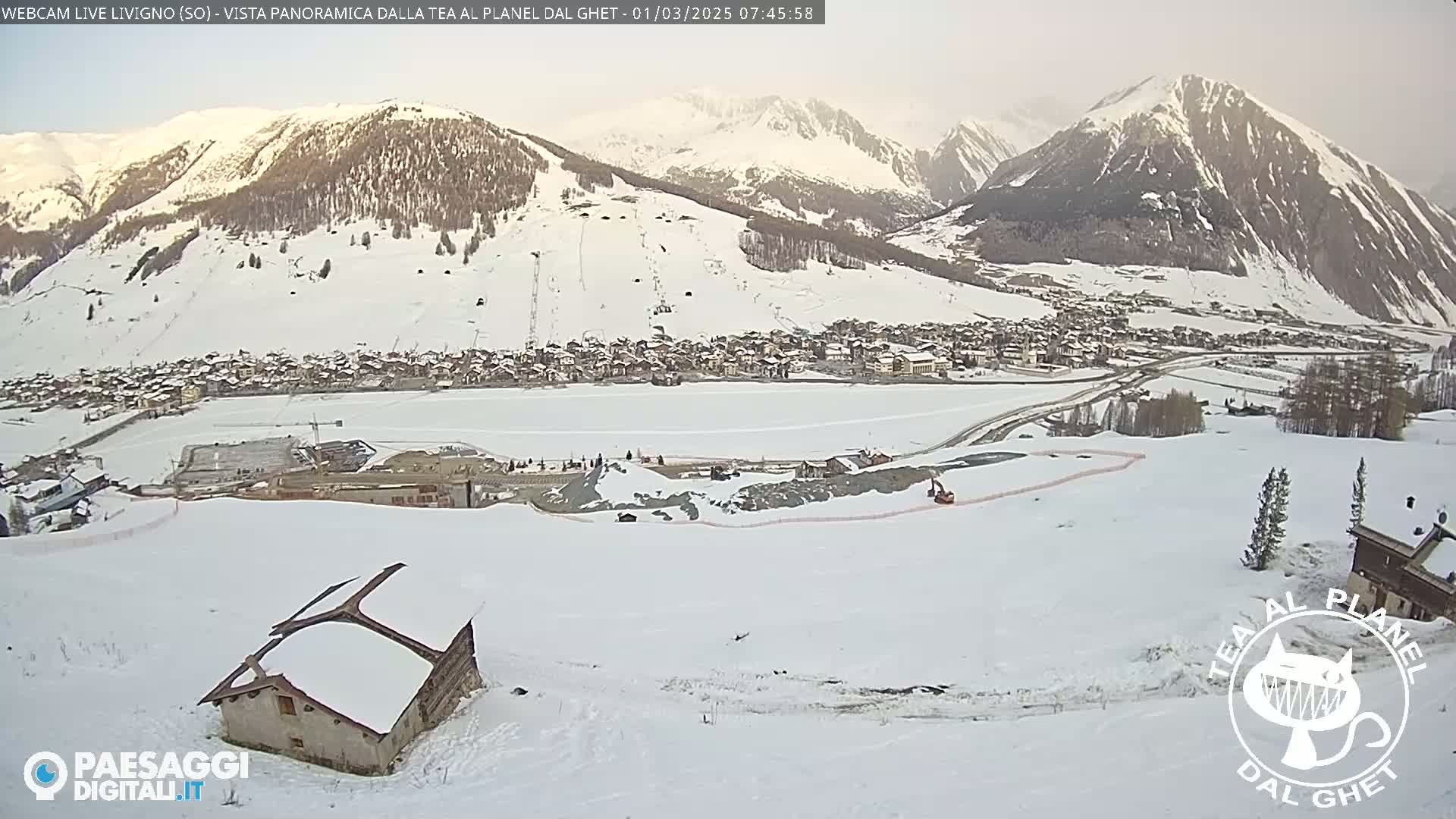 A snow-covered village nestled in a valley between snow-capped mountains under an overcast sky.