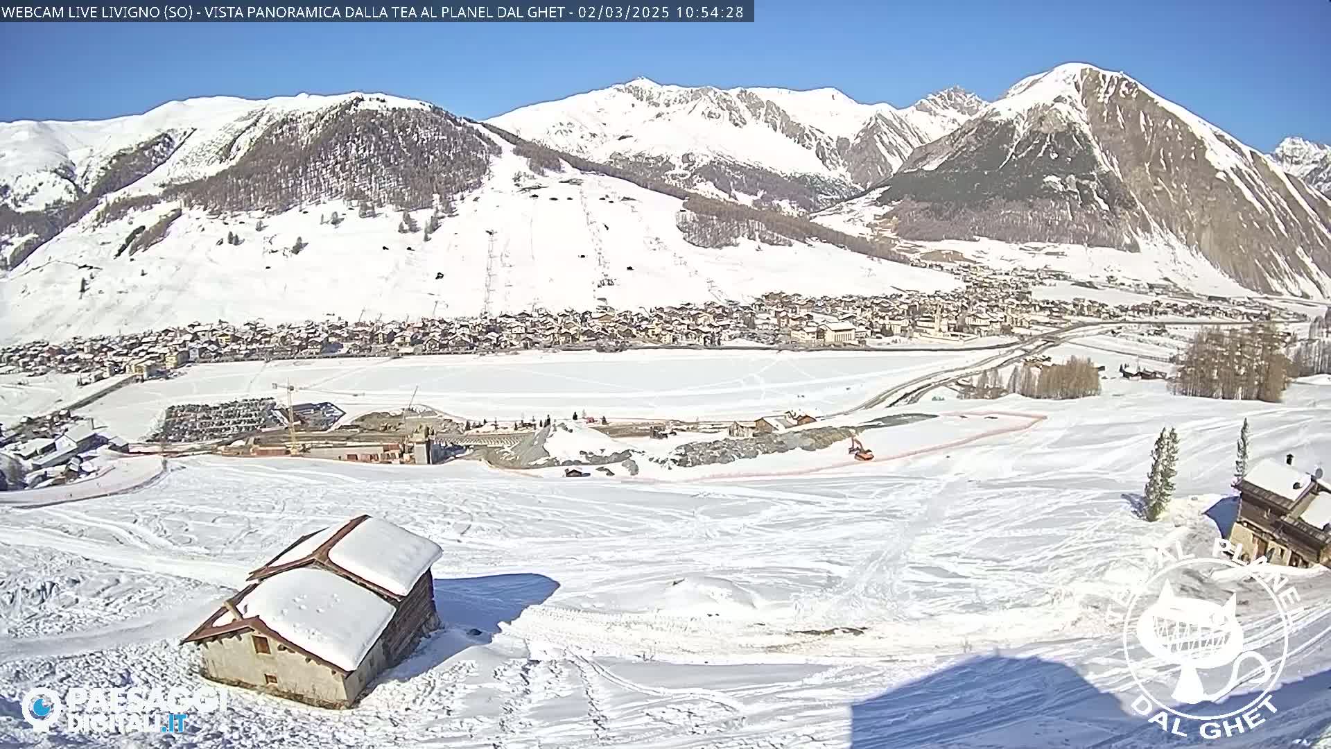 A snow-covered mountain village is nestled in a valley beneath snow-capped mountains on a sunny day.