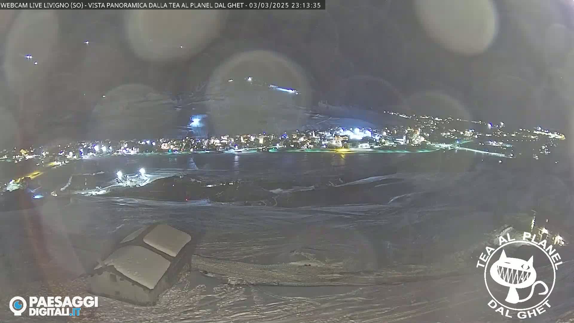 A nighttime, snowy, panoramic view of a town illuminated by lights, seen from a high vantage point.