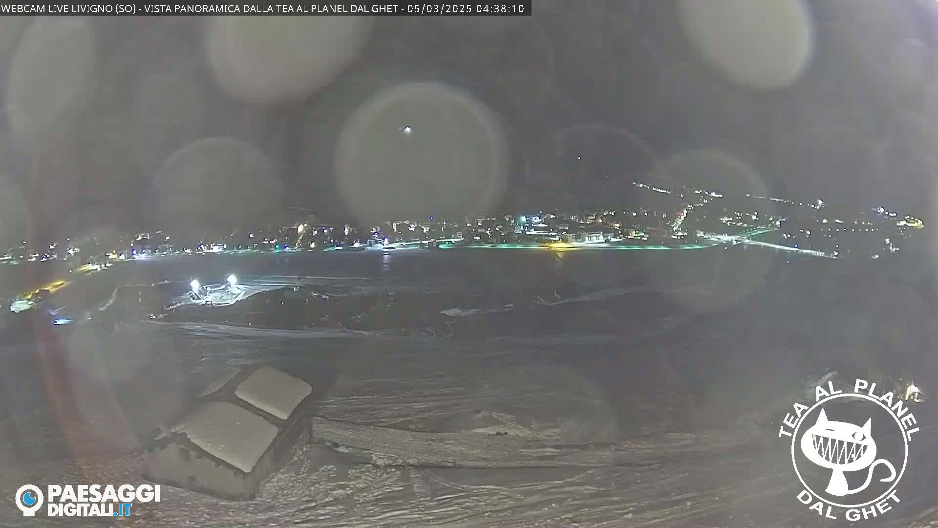 A nighttime, snowy landscape overlooking a town illuminated by lights, with a hazy atmosphere.