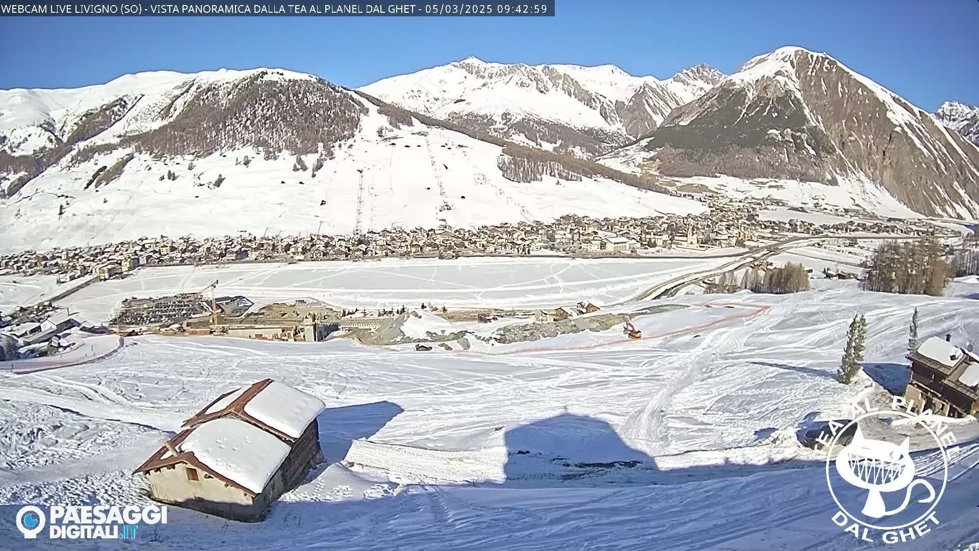 A snow-covered mountain valley town is visible beneath a sunny sky, with a frozen lake and ski slopes in the foreground.