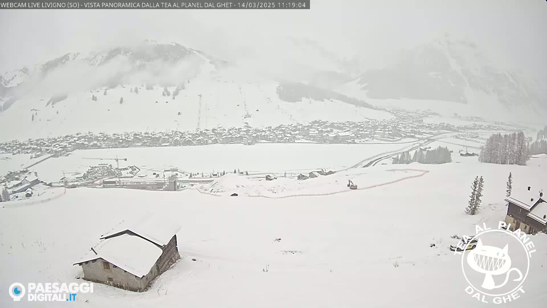 A snow-covered landscape shows a village nestled in a valley beneath snow-dusted mountains during a heavy snowfall.