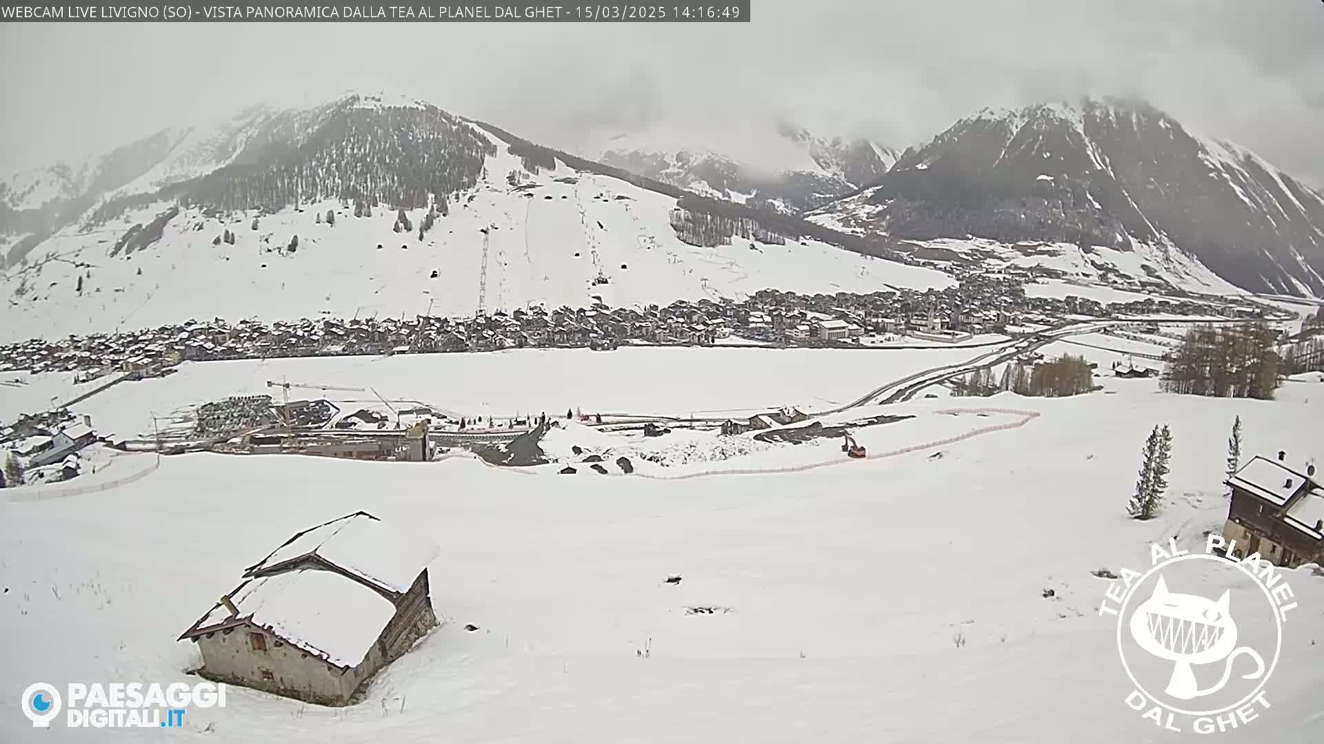 A snow-covered village nestled in a valley between snow-capped mountains on an overcast day.