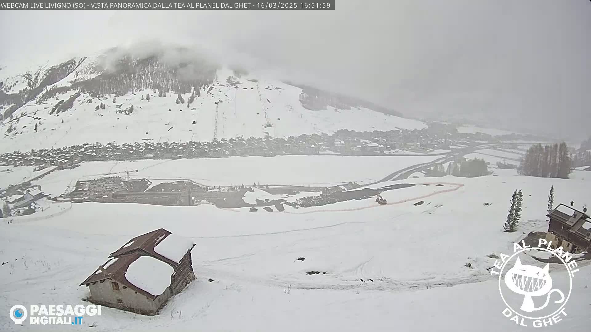 A snow-covered landscape, shrouded in fog, shows a small village nestled in a valley below a mountain, with a lone building in the foreground.