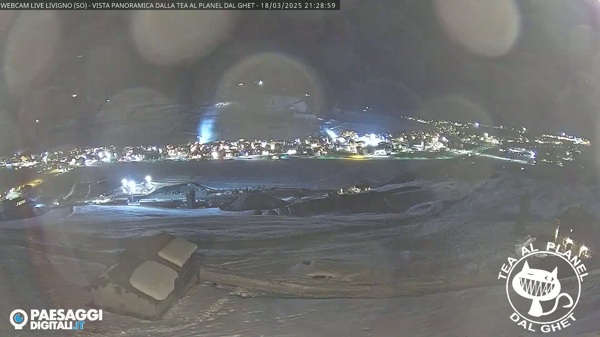 A nighttime, panoramic view of a snow-covered town illuminated by lights, with a dark, possibly cloudy sky above.