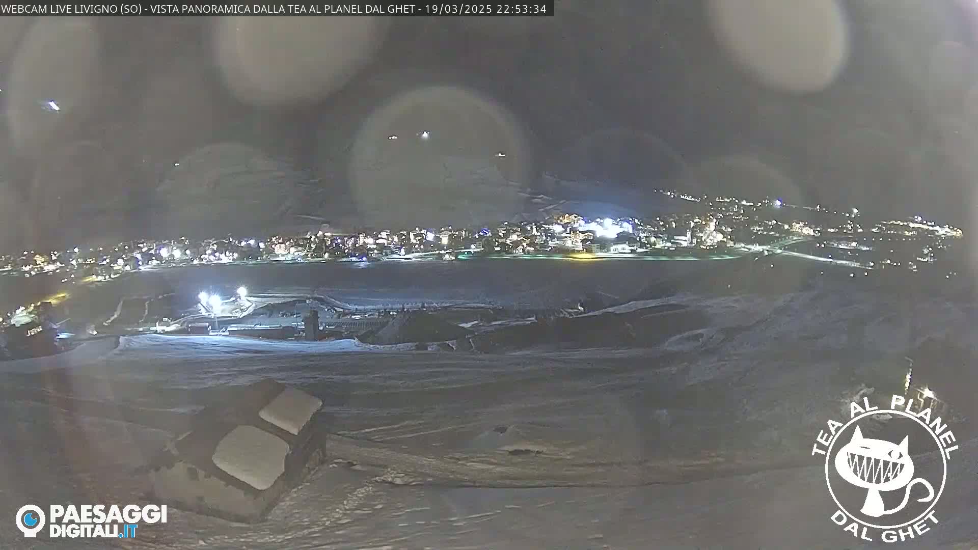 A nighttime, snowy panorama shows a town illuminated below, with a snow-covered landscape in the foreground.
