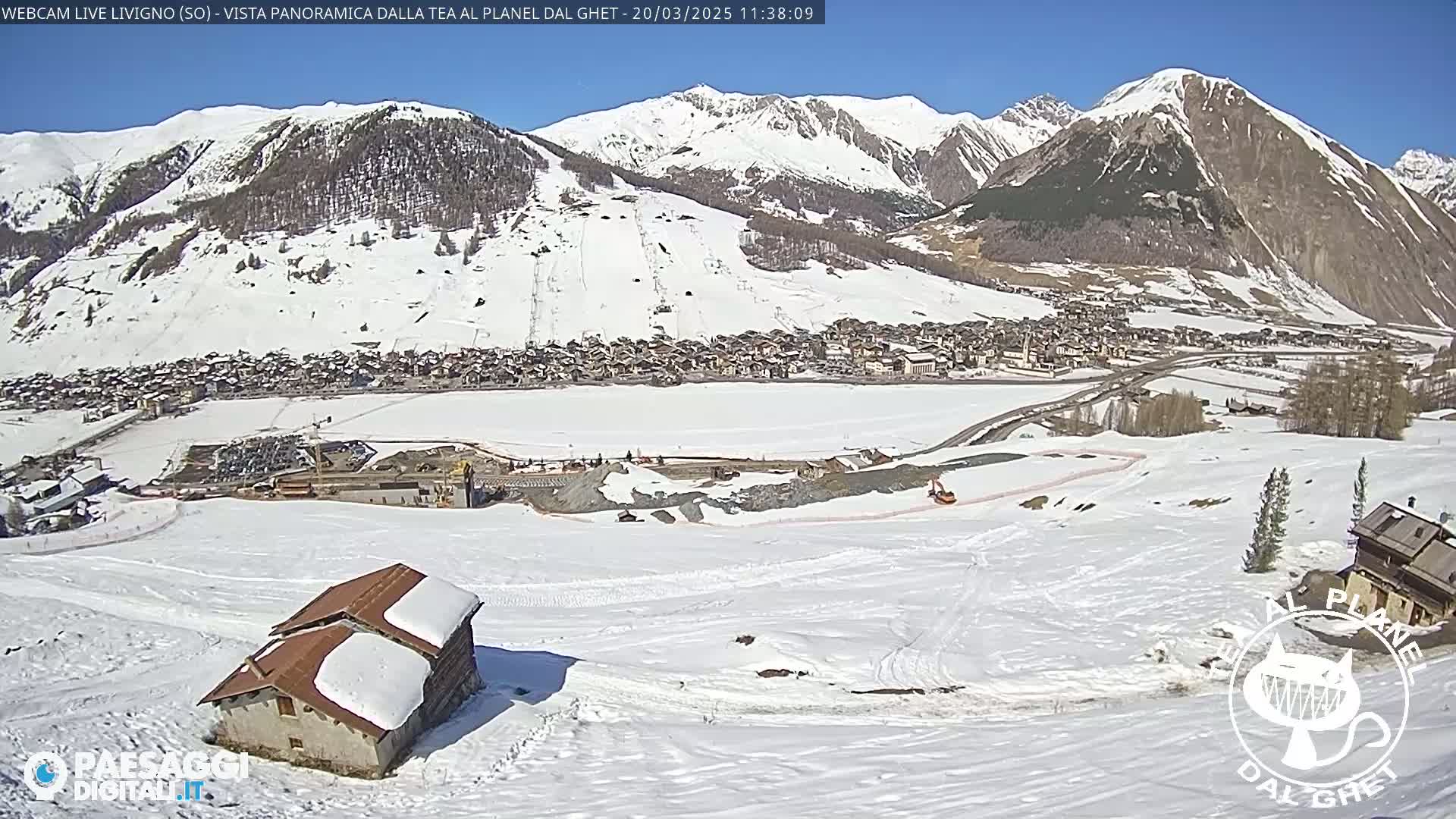 A snow-covered mountain village is visible beneath a bright, sunny sky, with a small house and some construction equipment in the foreground.