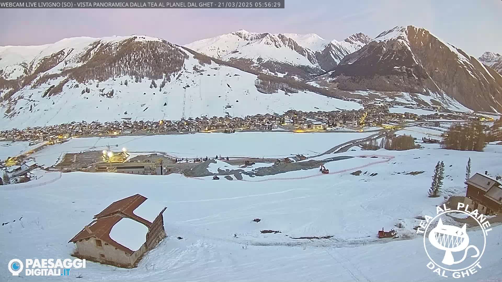 A snow-covered mountain village is nestled in a valley at dusk, with snow-covered mountains rising in the background.