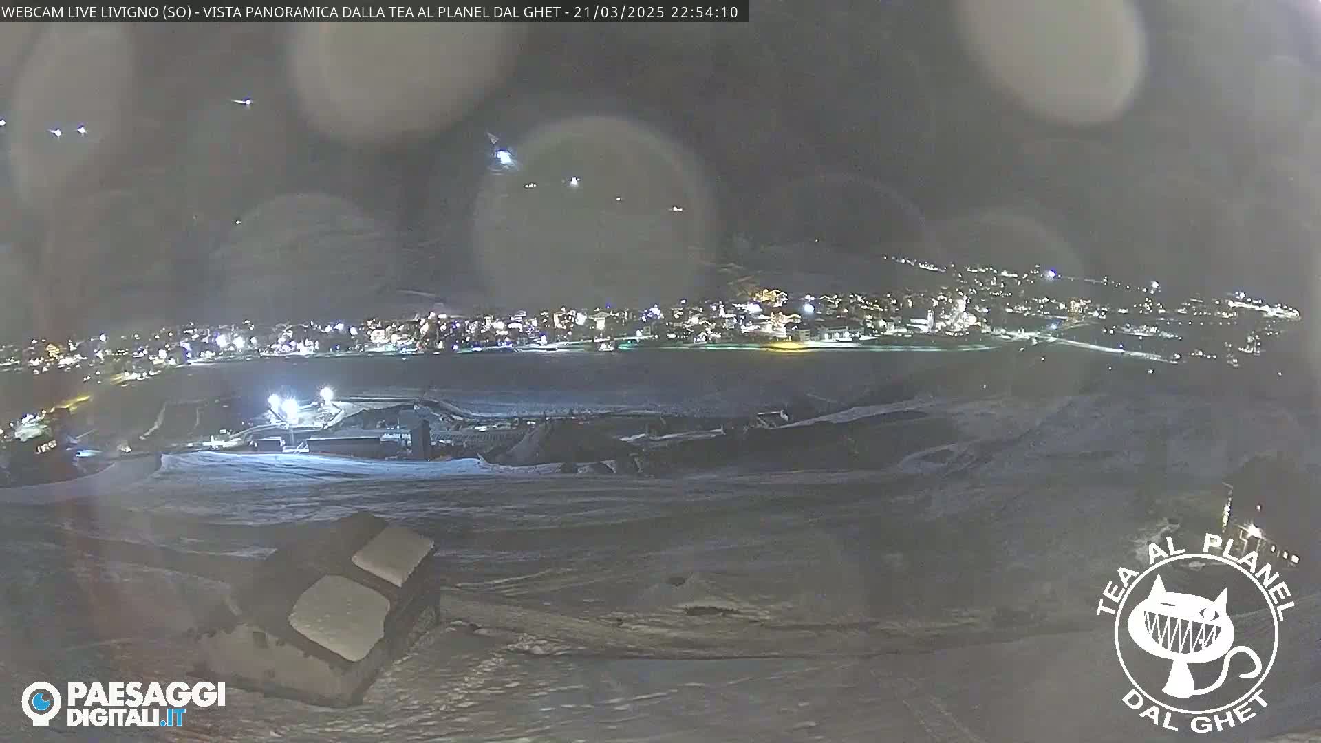 A nighttime, snowy panoramic view of a town illuminated by lights, seen from a high vantage point.