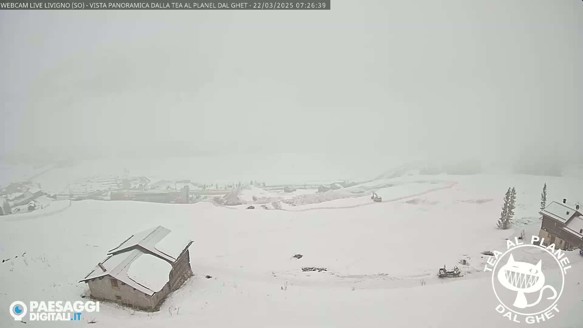 A snow-covered landscape with a small building in the foreground and a village in the distance under heavy snow.