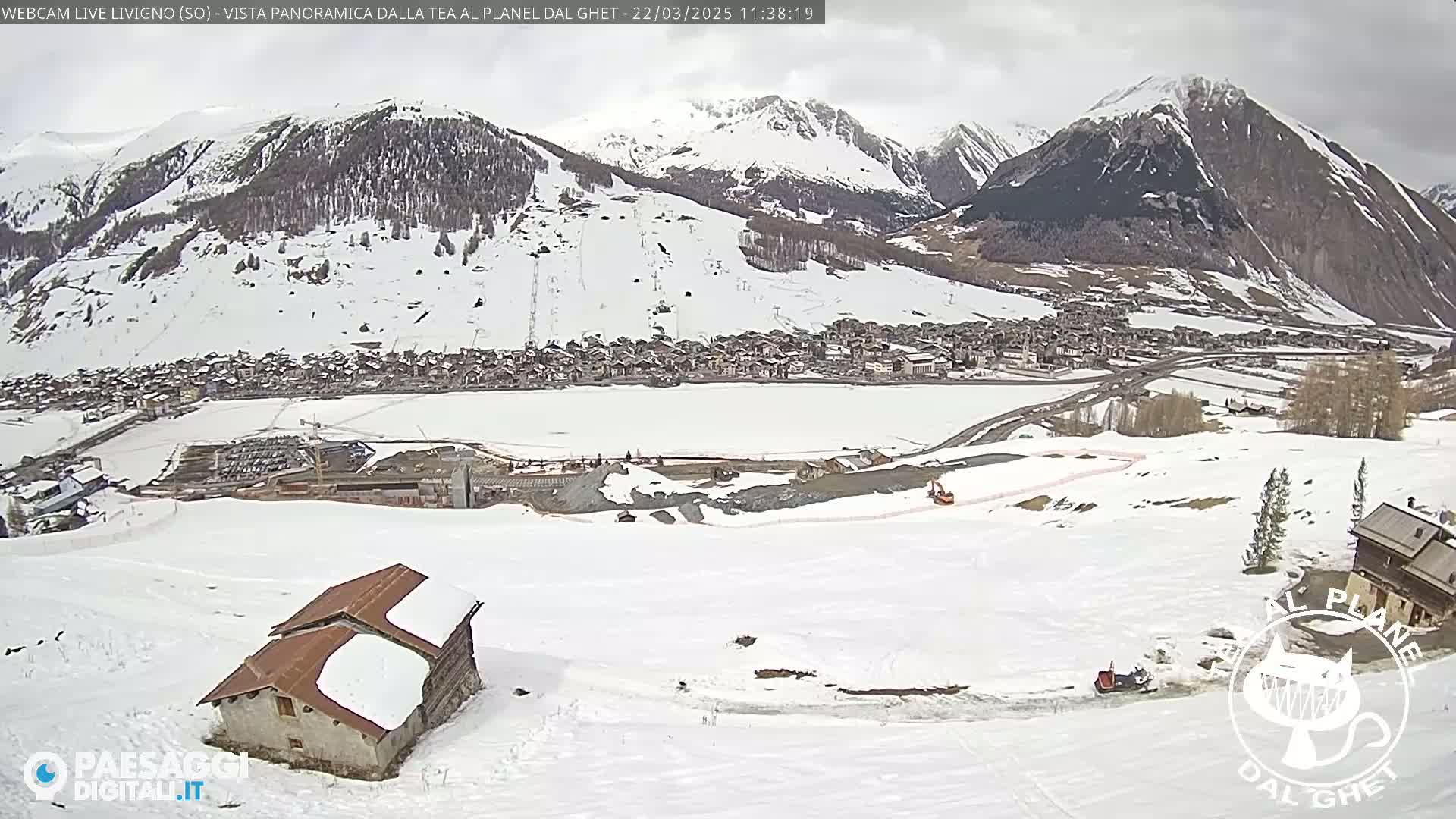 A snow-covered mountain village is seen from a high vantage point on a cloudy day, with a small building and some construction visible in the foreground.