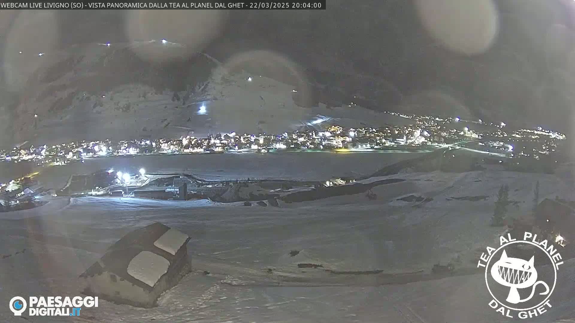 A nighttime, snowy landscape shows a town lit up in the distance, under a dark sky.