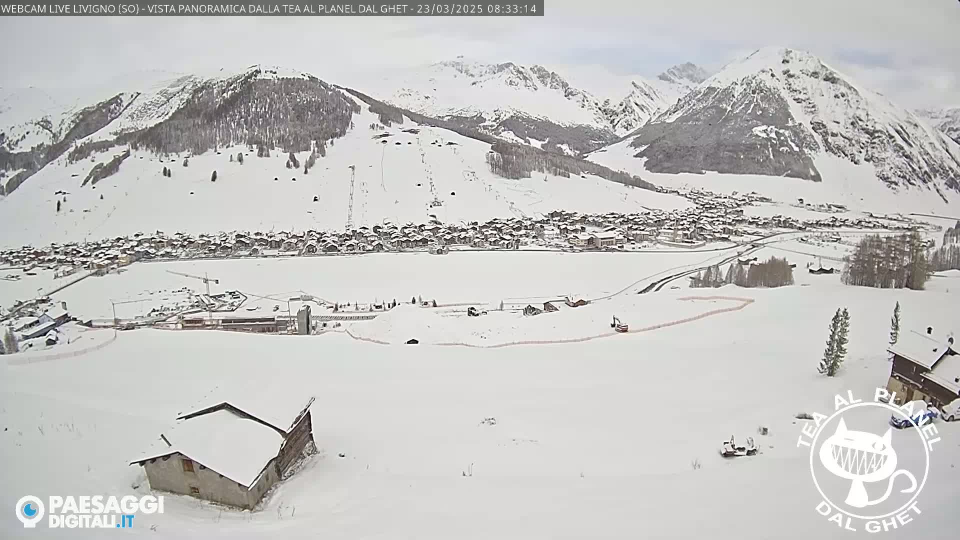 A snow-covered village nestled in a valley between snow-capped mountains under an overcast sky.