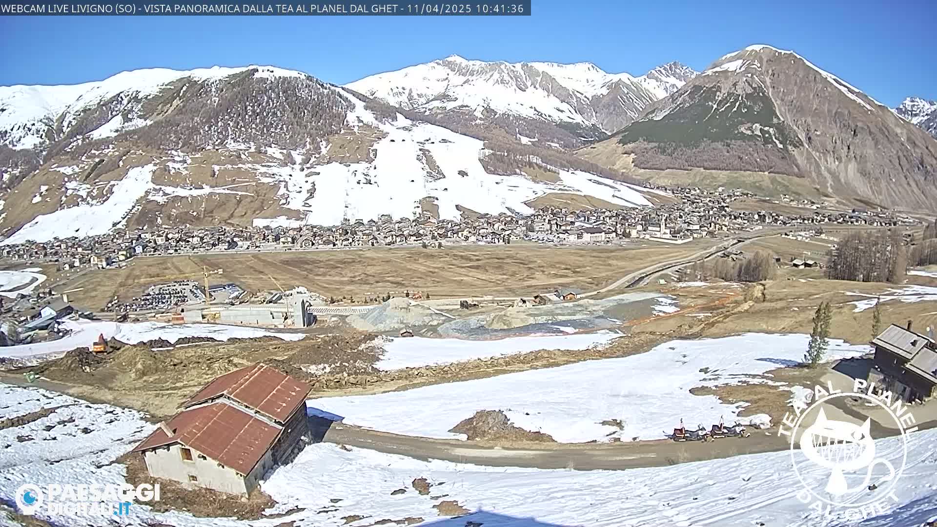 A panoramic view of a snow-dusted mountain town, partially under construction, on a sunny day.