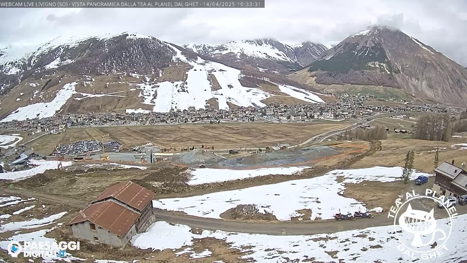 A mountain village nestled in a valley, partially snow-covered, under an overcast sky.