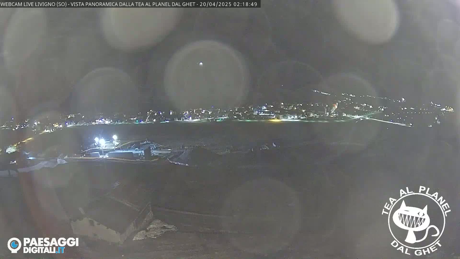 A nighttime, blurry panoramic view of a town lit up under a hazy sky shows a dark, snowy foreground.