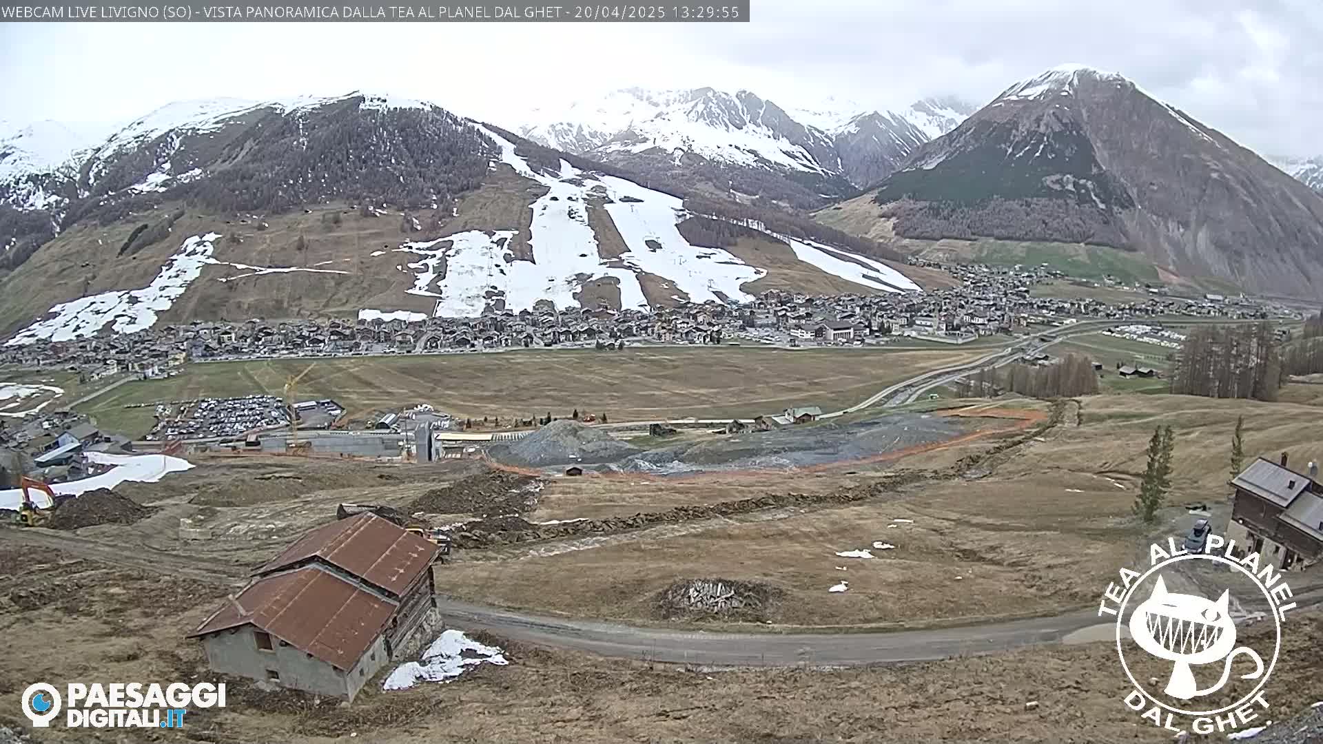 A mountain town nestled in a valley, partially snow-covered mountains in the background, under an overcast sky.