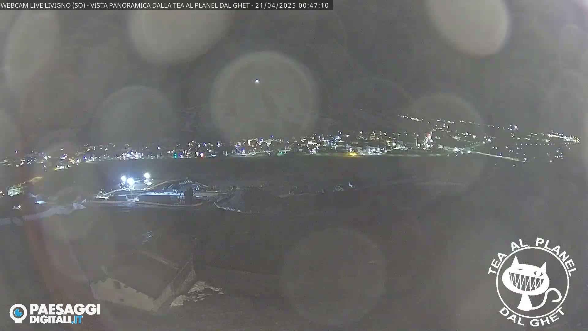 A nighttime, hazy long shot of a town illuminated with lights across a dark landscape.