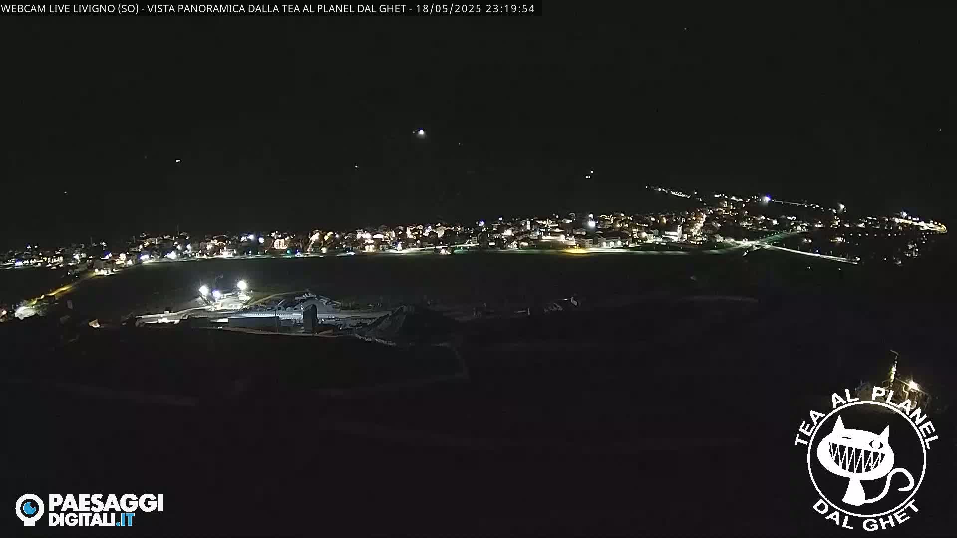 A nighttime, aerial view shows a small town illuminated with lights under a clear, dark sky.