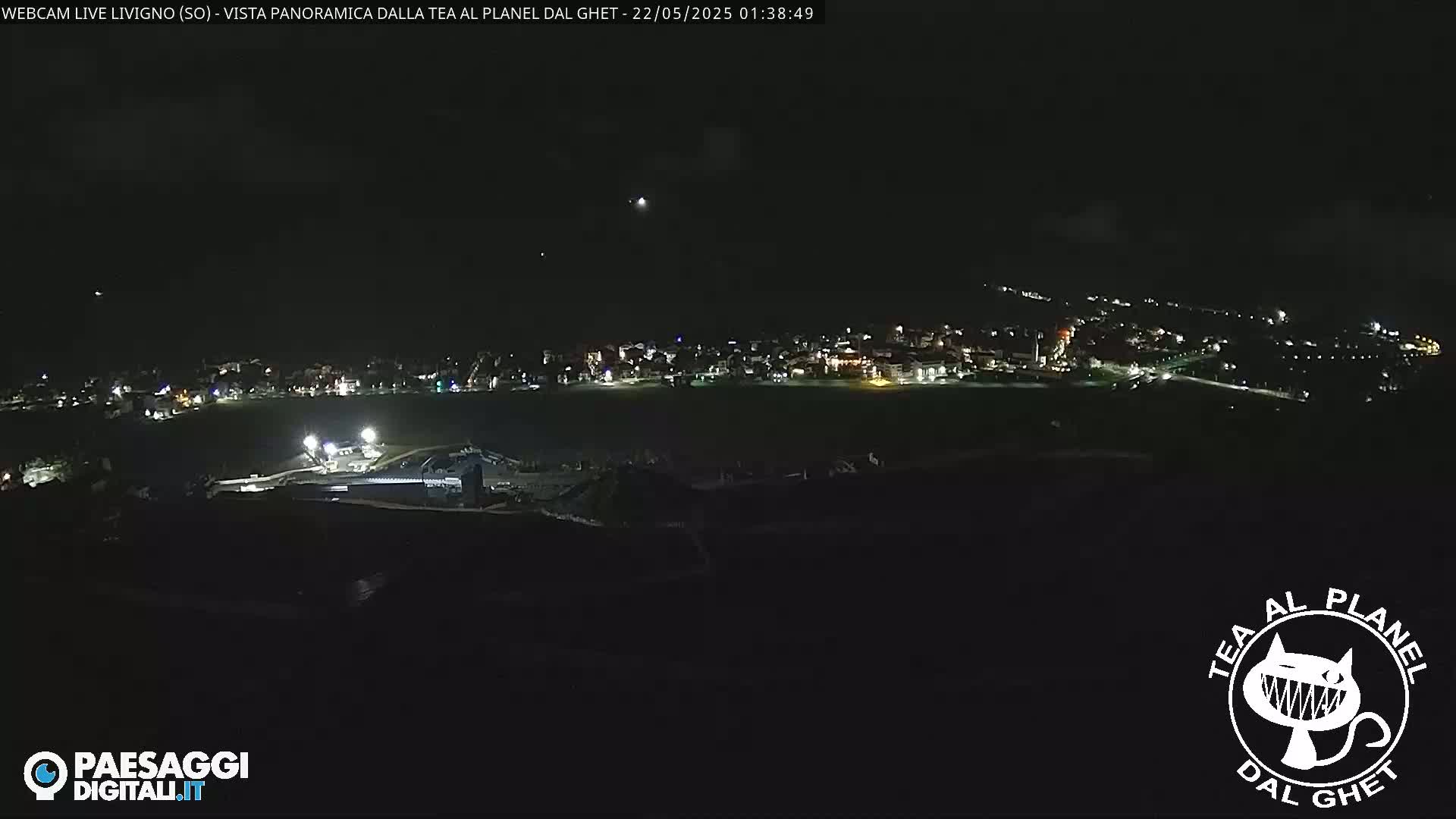A nighttime long shot shows a town's lights spread across a dark landscape under a clear sky.