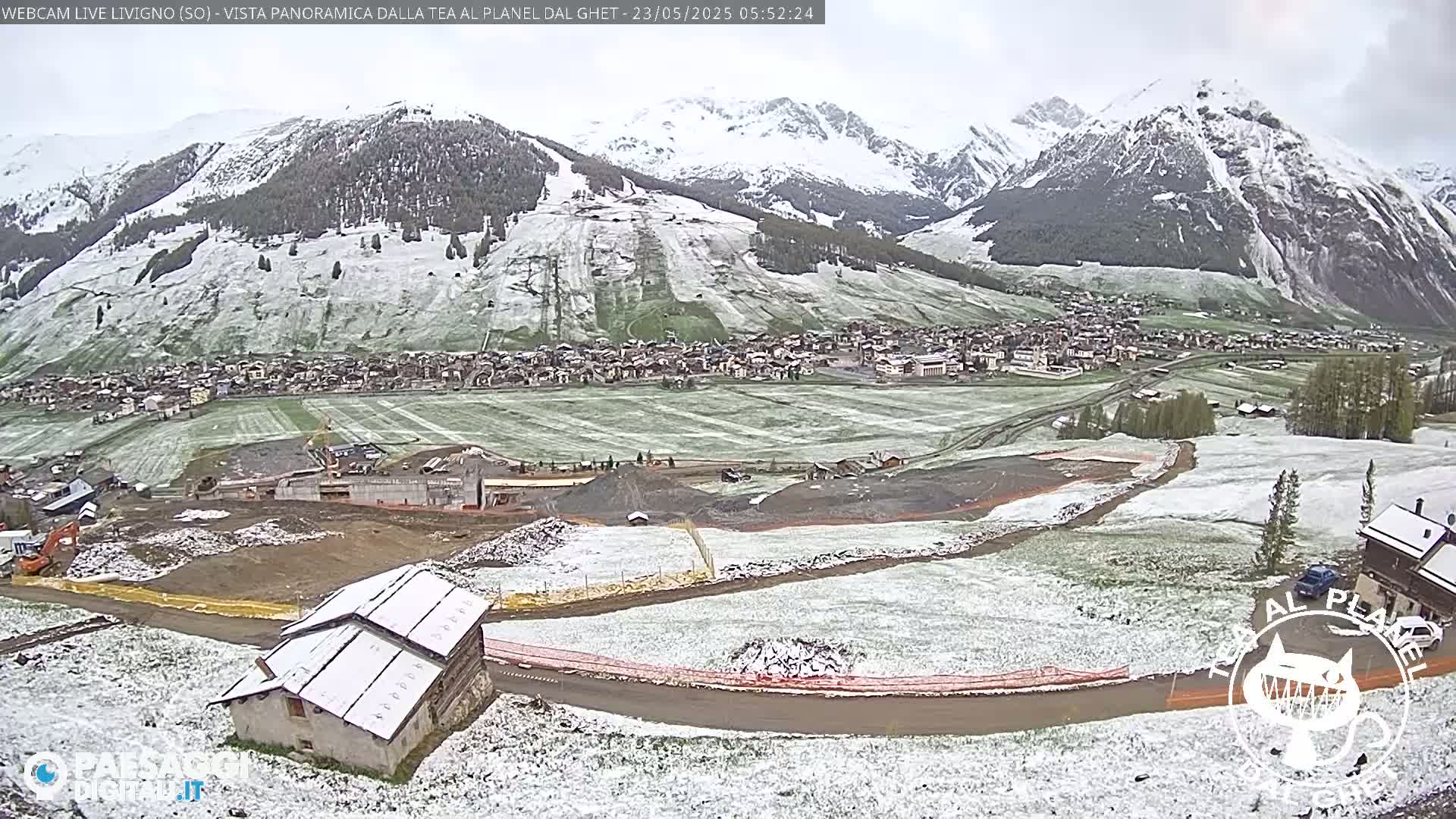 A snow-dusted mountain village is nestled in a valley surrounded by snow-capped mountains under a cloudy sky.