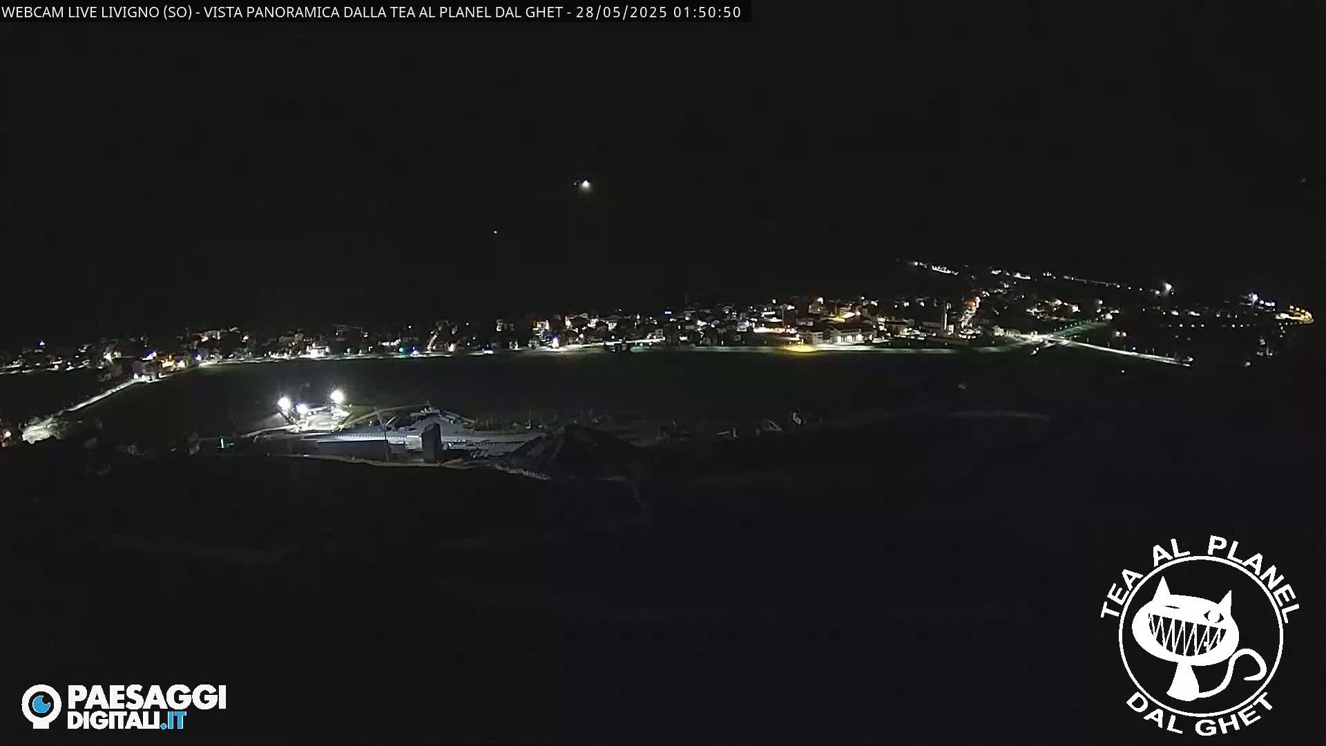 A nighttime, panoramic view of a small town illuminated by scattered lights, seen from a high vantage point.