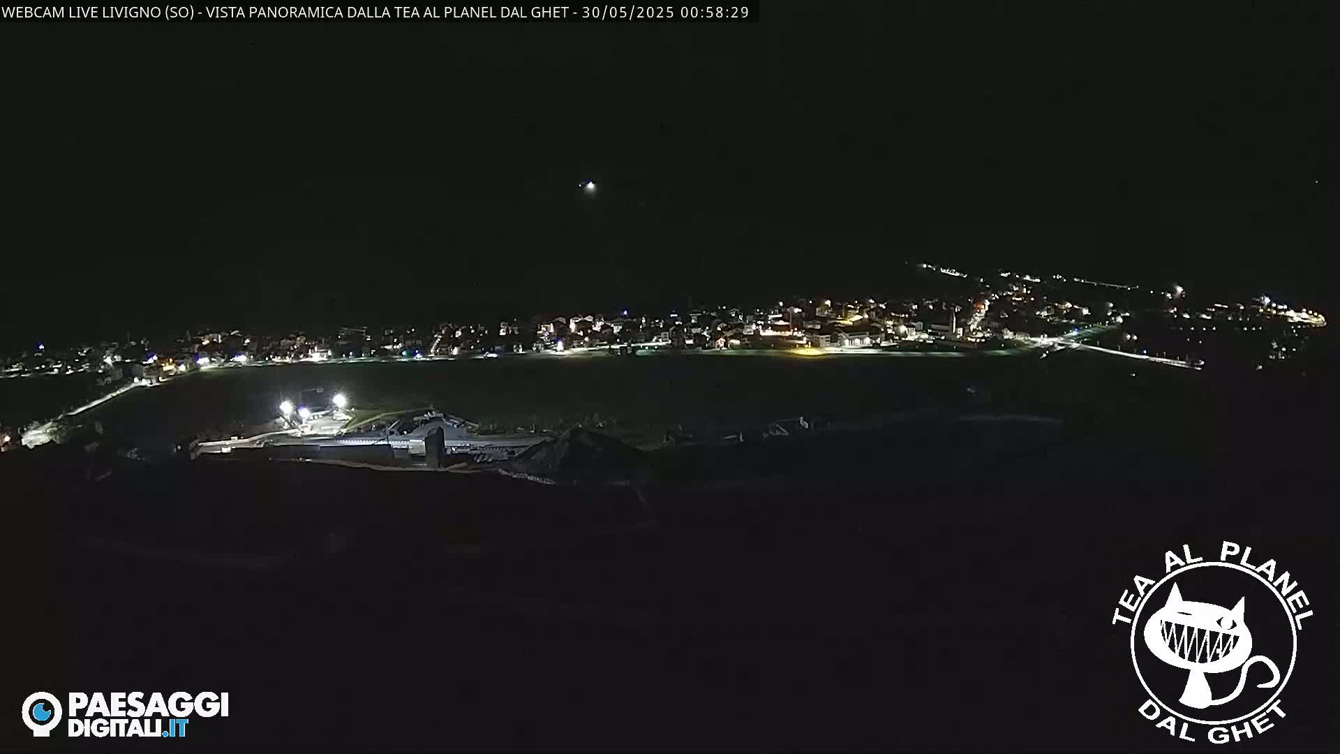 A nighttime, panoramic view of a small town illuminated by scattered lights under a clear, dark sky.