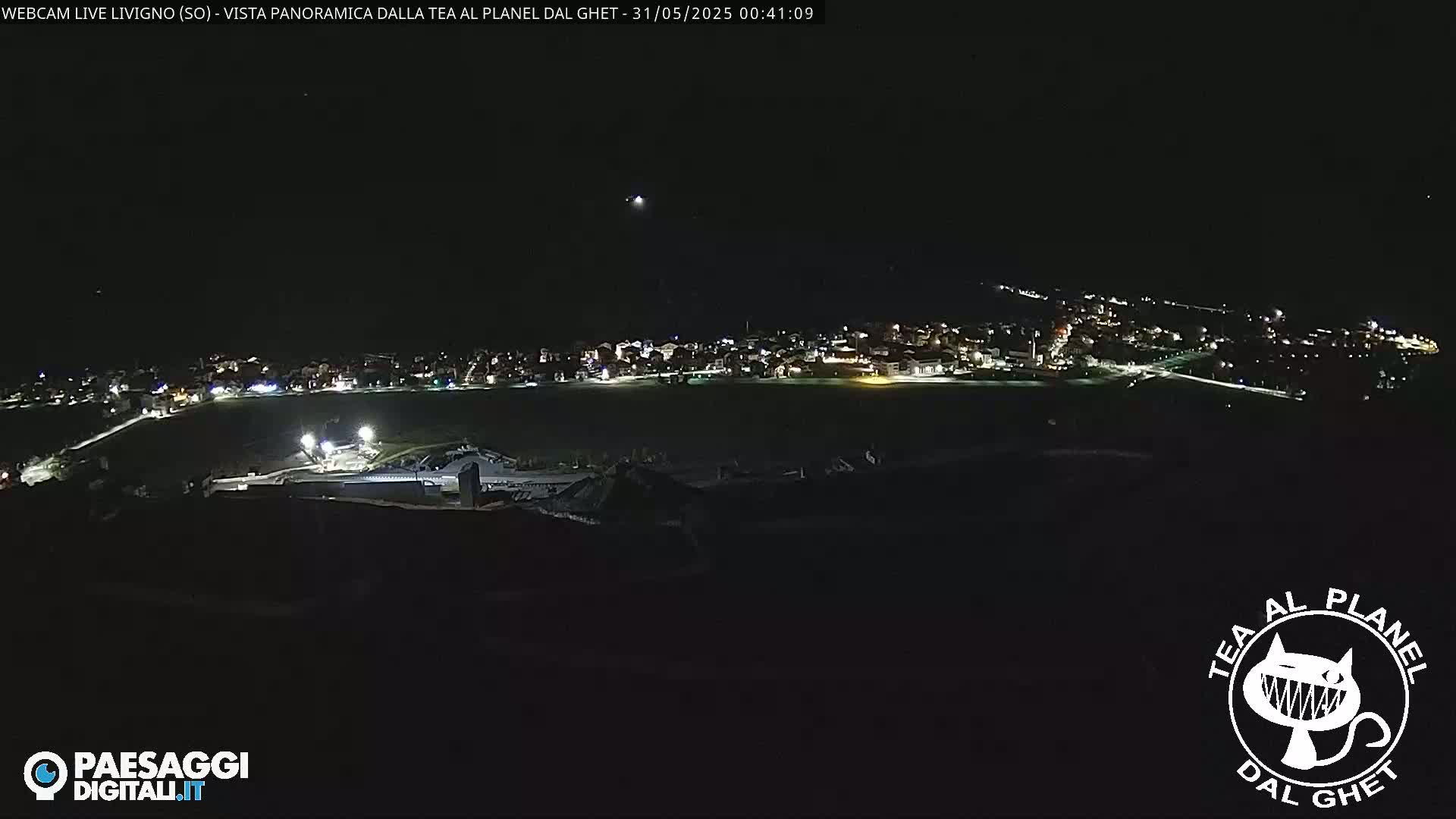 A nighttime, panoramic view of a town illuminated by lights, situated in a dark, open area under a clear sky.
