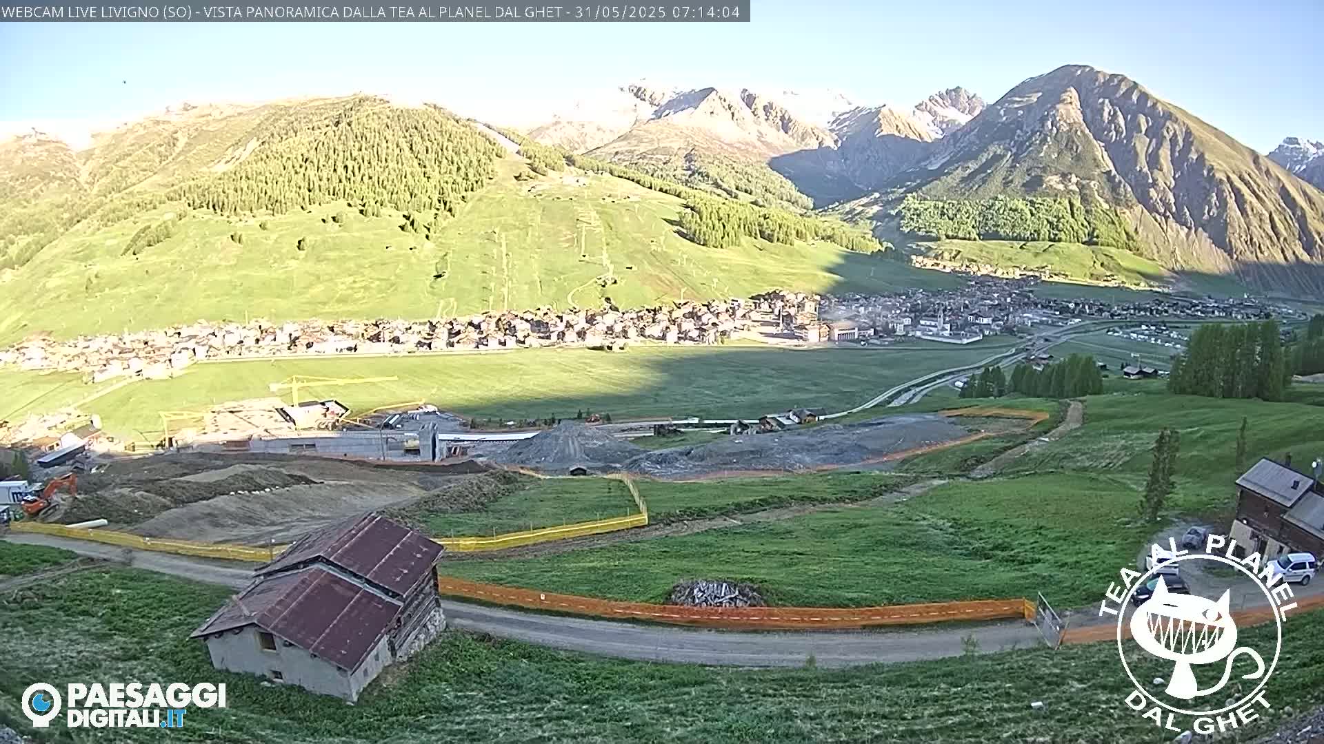 A sunny mountain town nestled in a valley, with construction visible in the foreground and snow-capped mountains in the background.