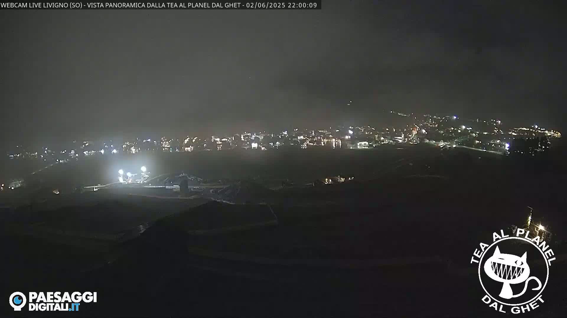 A nighttime, panoramic view of a snow-covered town with faint lighting, under a dark, cloudy sky.