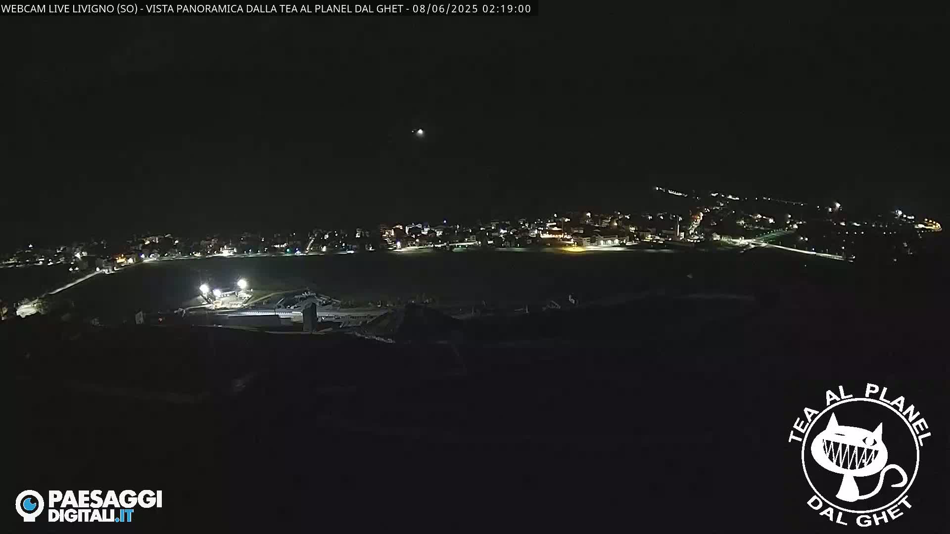 A nighttime long shot shows a dimly lit town spread across a dark landscape under a clear sky.