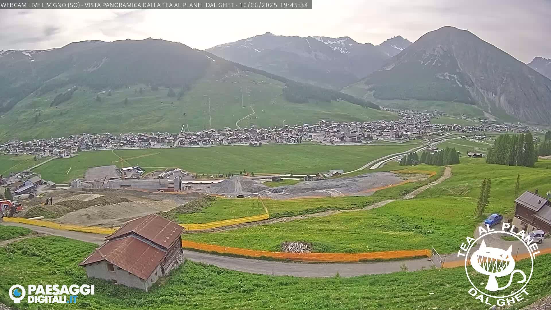 A mountain village nestled in a valley, under a partly cloudy sky, with ongoing construction visible in the foreground.