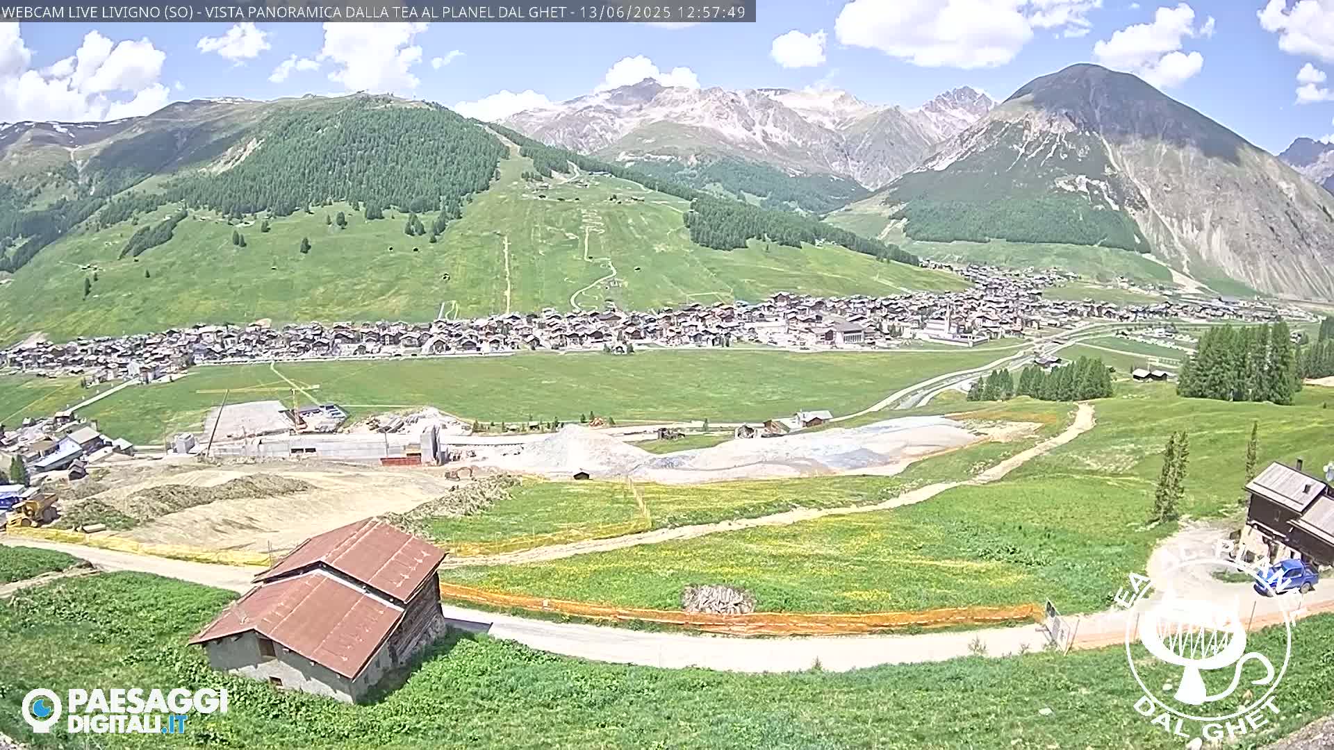 A sunny mountain valley town is visible, with construction underway in the foreground, under a partly cloudy sky.