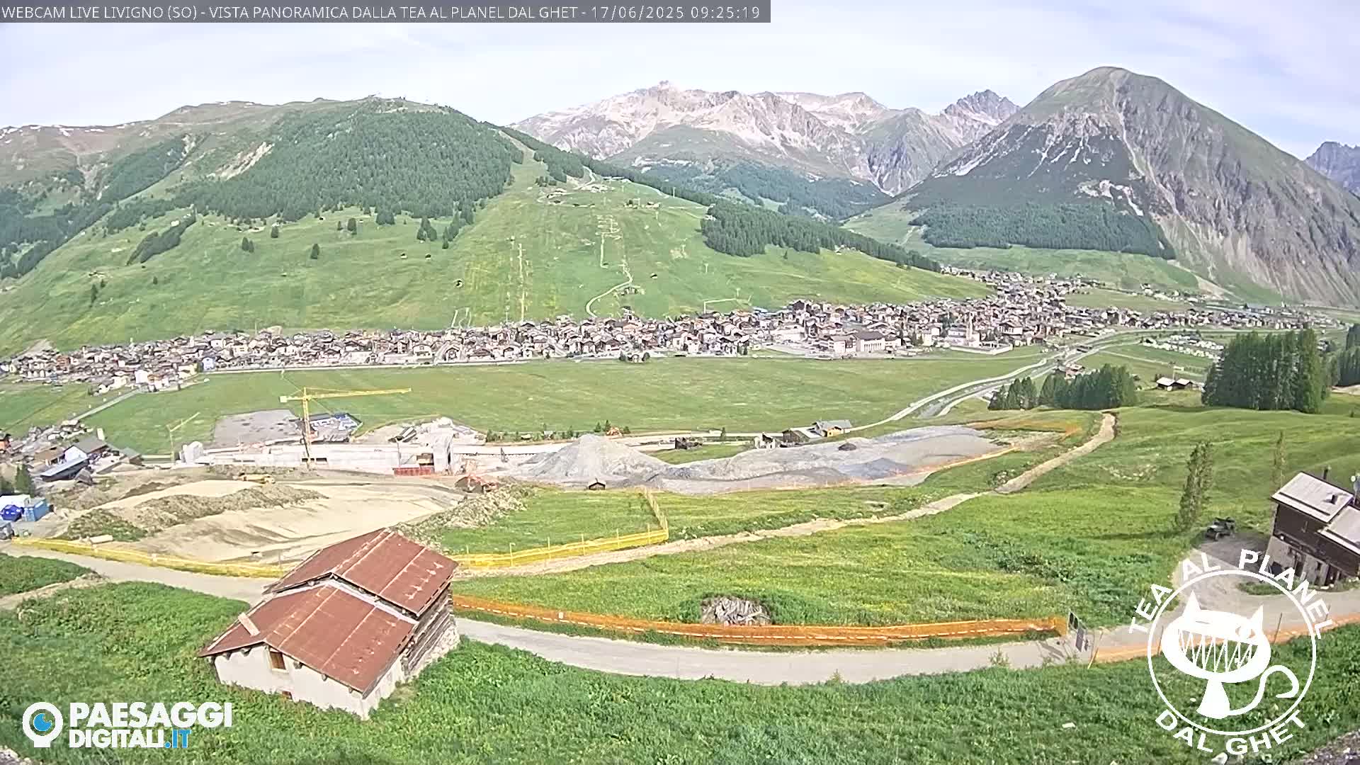 A mountain town nestled in a valley, with construction visible in the foreground, under a mostly clear sky.