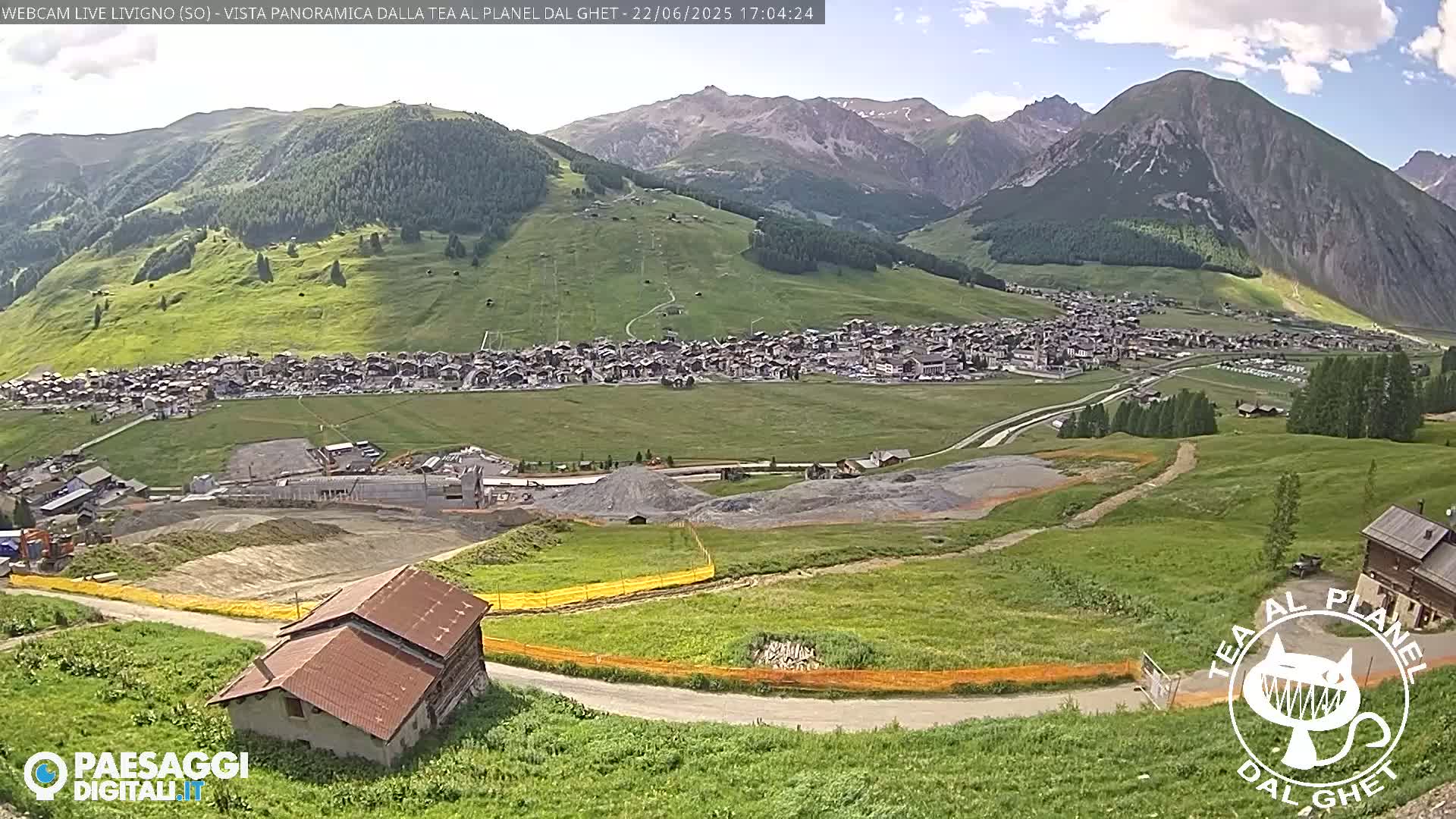 A mountain village nestled in a valley, surrounded by green hills and mountains under a partly cloudy sky.