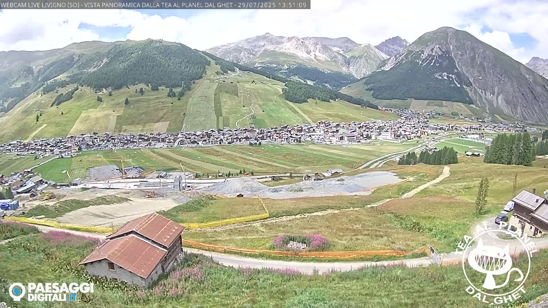 A sunny mountain valley town is visible, with construction taking place in the foreground, and snow-capped mountains in the background.