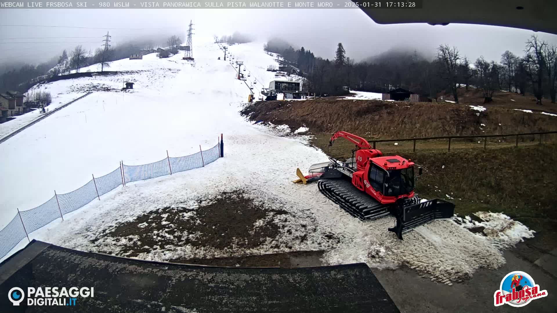 A red snowcat sits on a snowy hillside next to a ski lift, under an overcast sky.