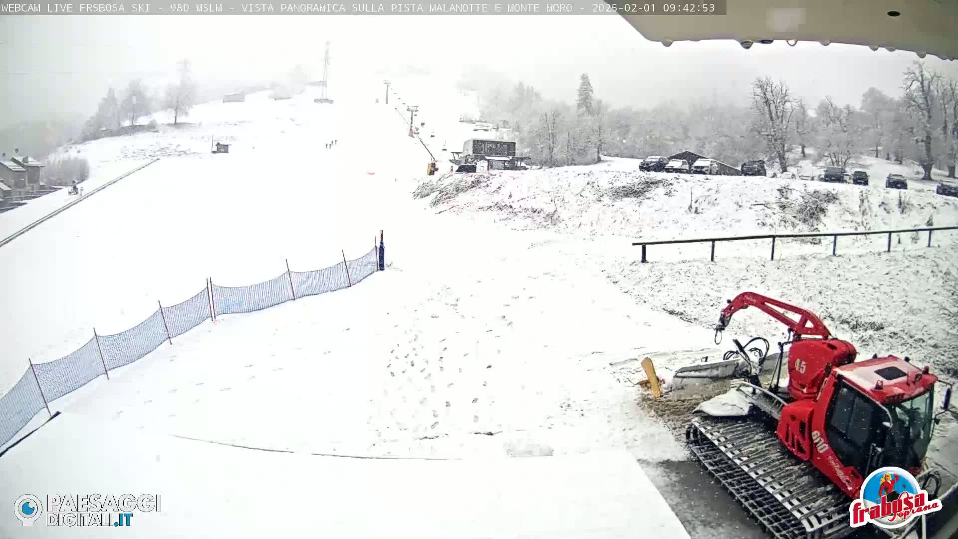 A snow-covered ski slope with a red snowcat is seen during a snowfall.