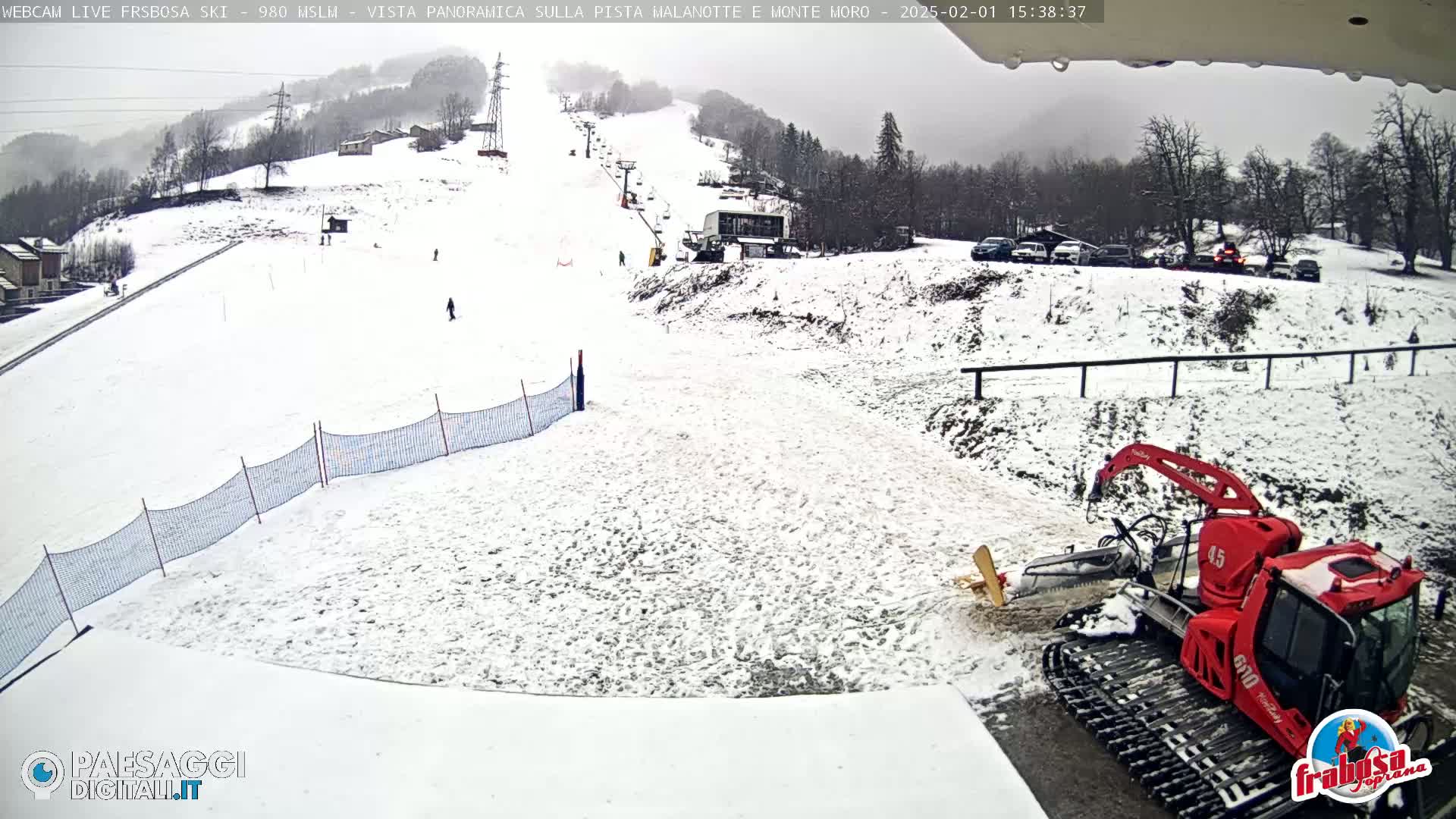 A snow-covered ski slope with a snow groomer parked near the bottom, under an overcast sky.
