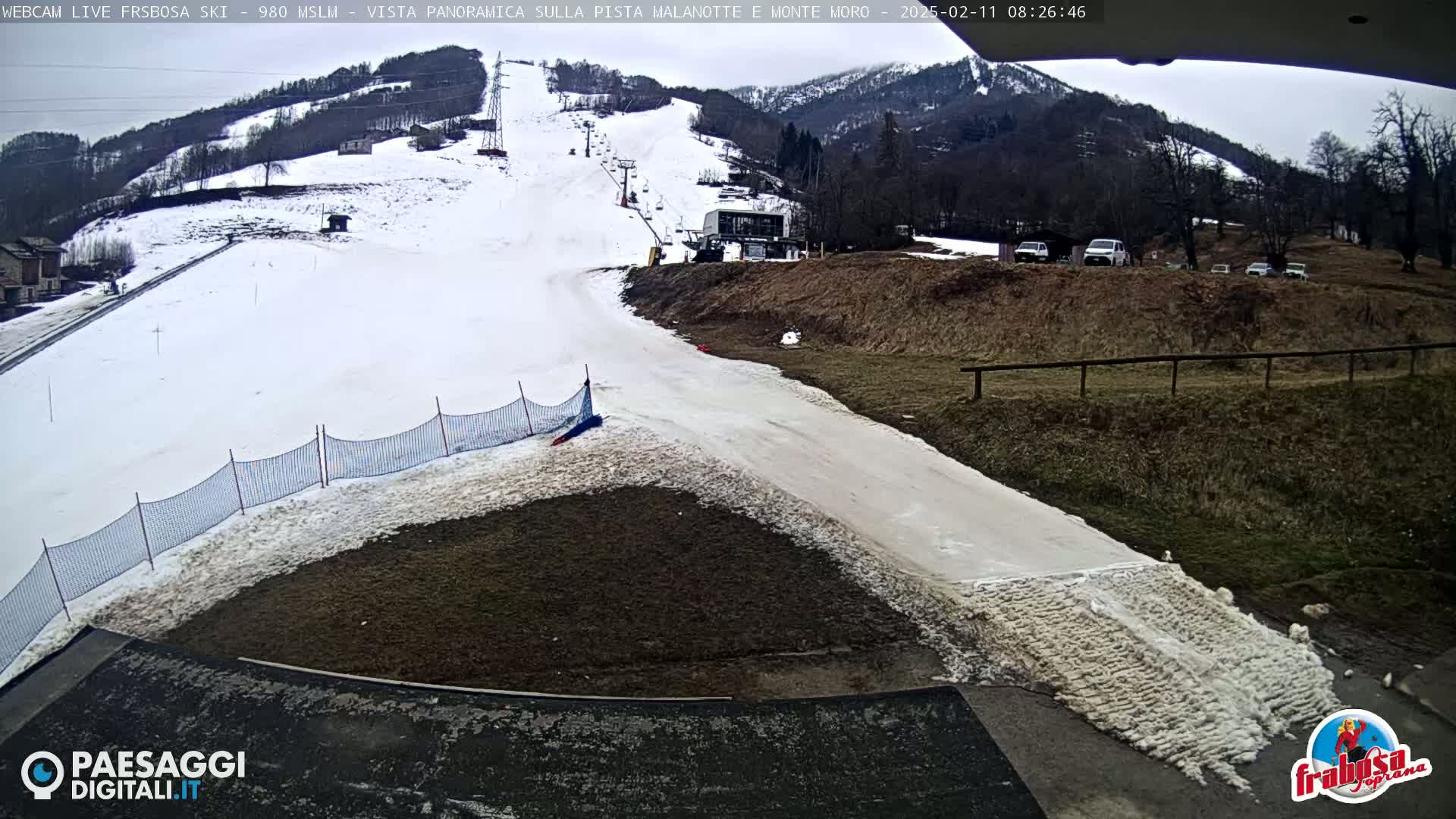 A snow-covered ski slope with a ski lift and several cars parked nearby under an overcast sky.