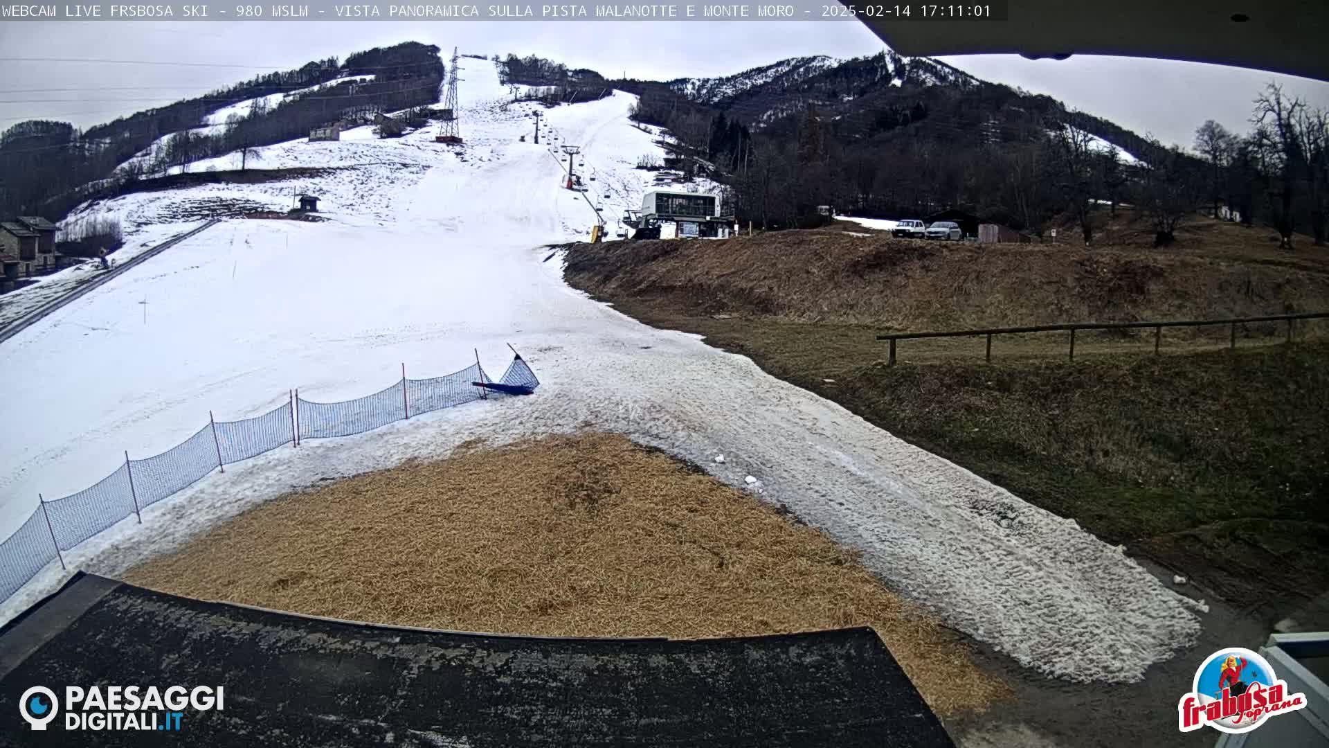 A snowy ski slope with a lift and a grassy area below it under an overcast sky.