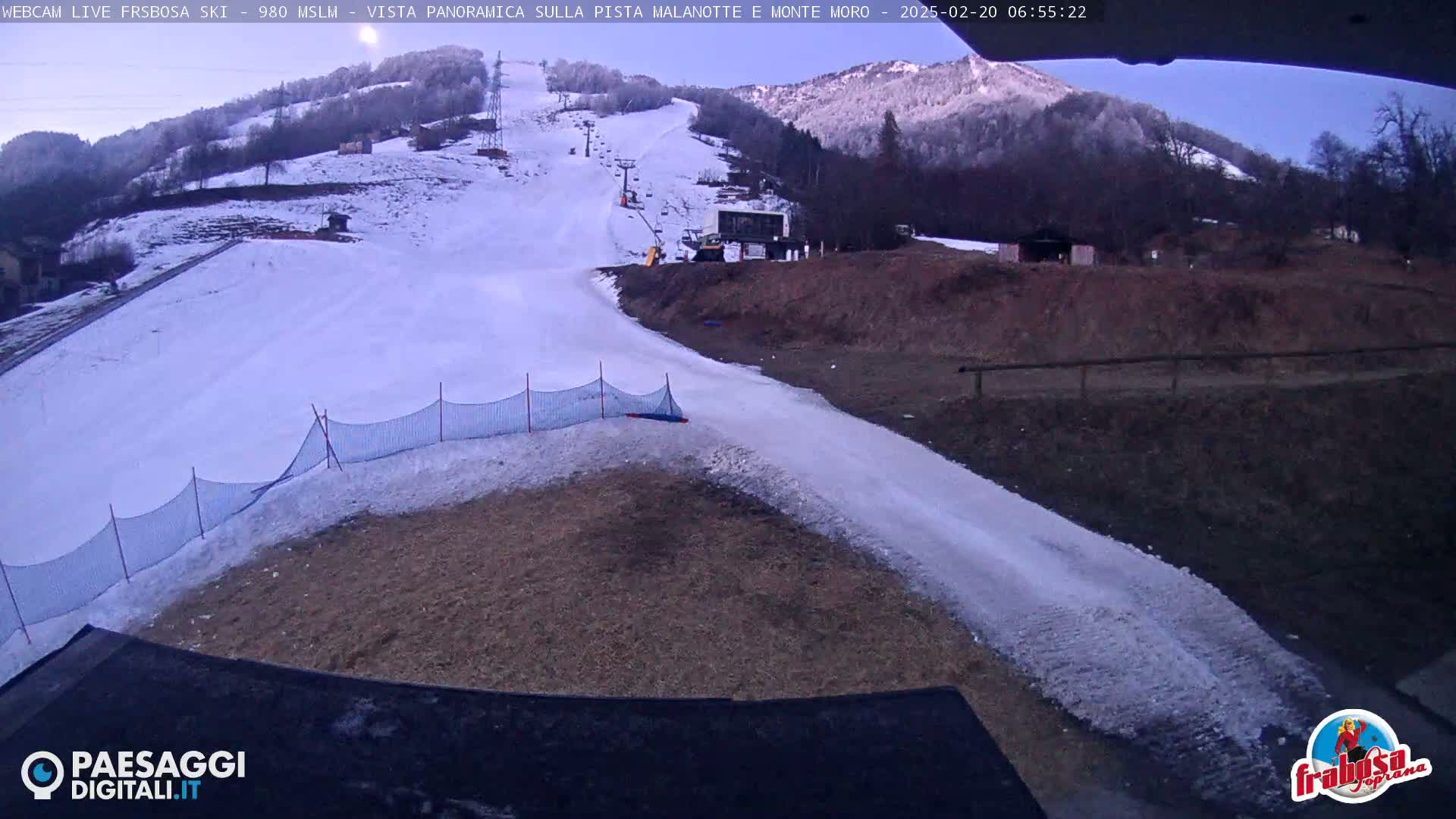 A snow-covered ski slope with a ski lift and some machinery is visible under a clear, twilight sky.