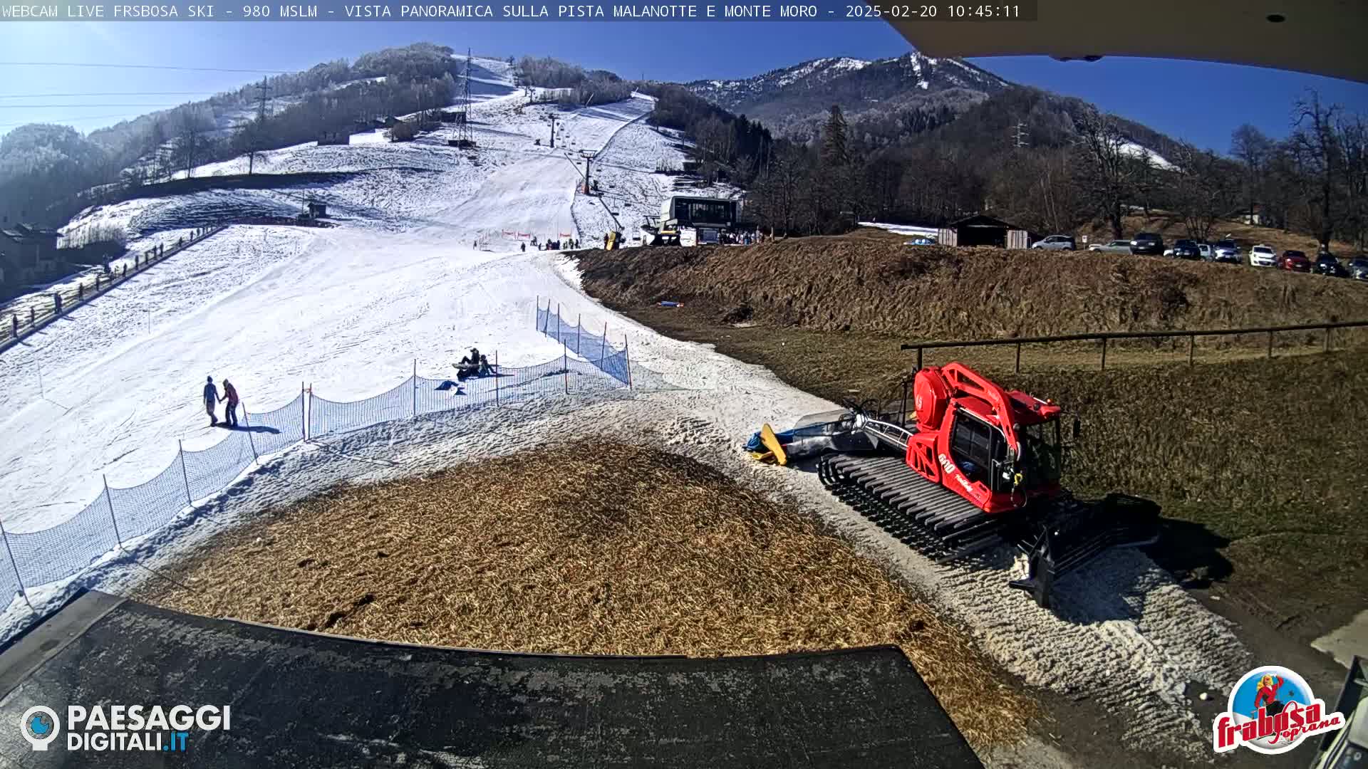 A snow-covered ski slope with a red snowcat parked at the bottom on a sunny day.