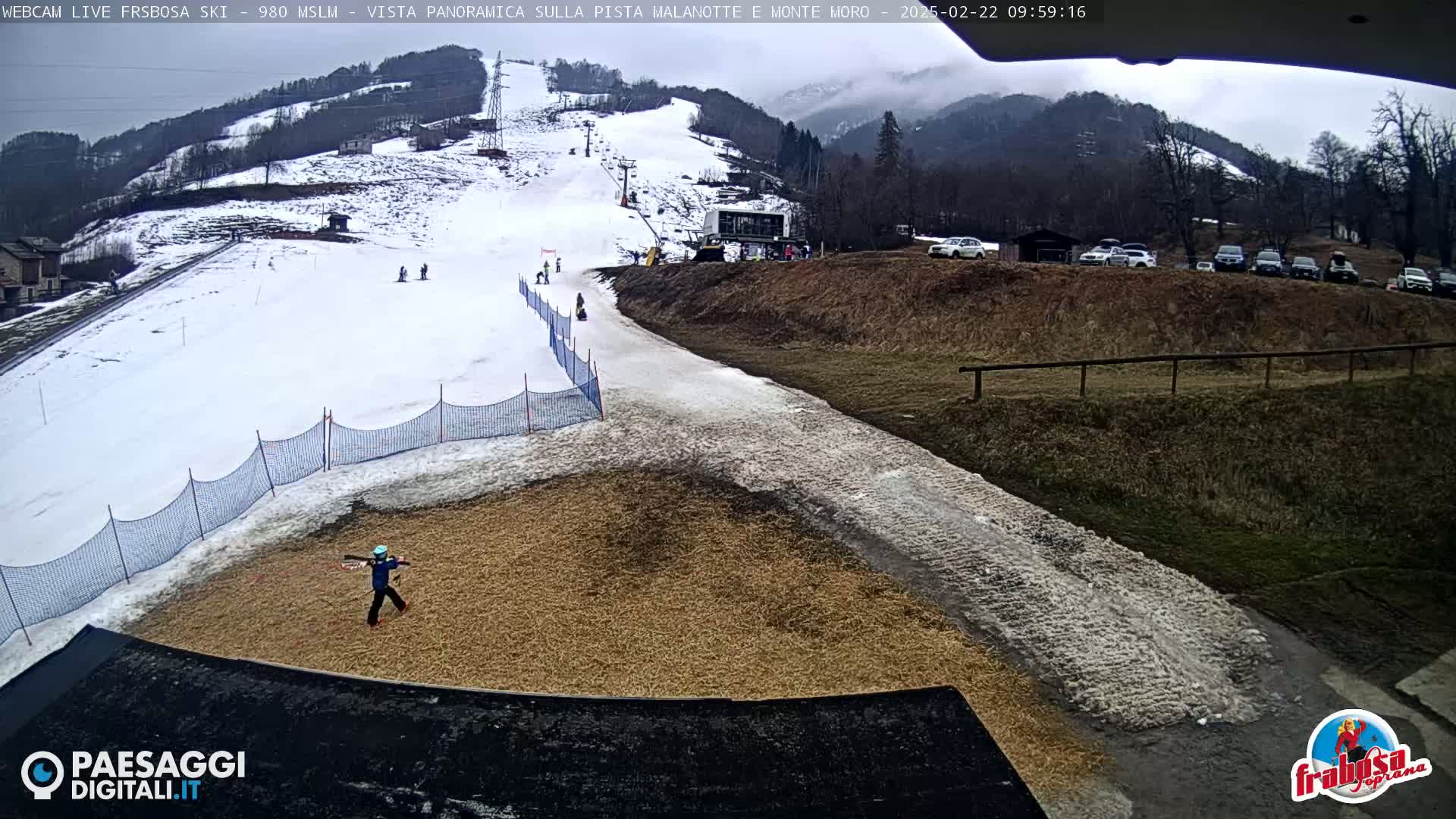 A snowy ski slope with a person on a tan area at the bottom, under an overcast sky.